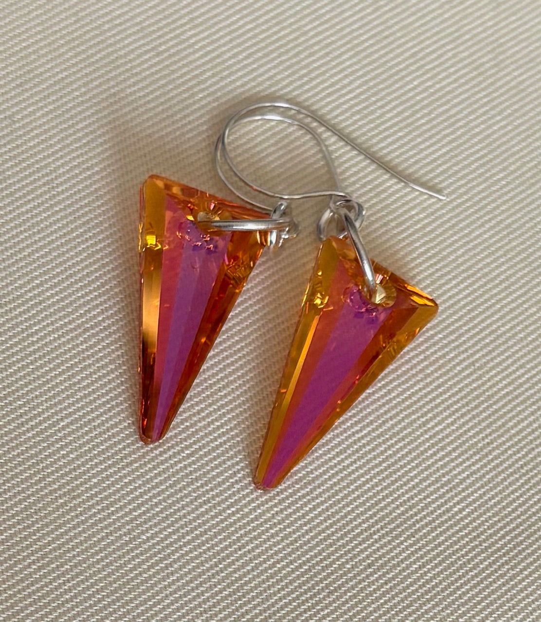 Triangular earrings with orange and pink gradient on a beige background