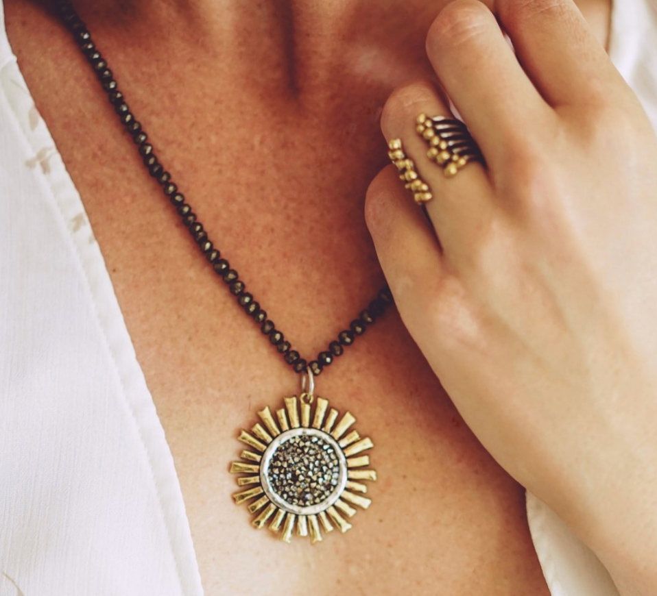 Close-up of a necklace with a sun-shaped pendant and a hand wearing a gold ring.