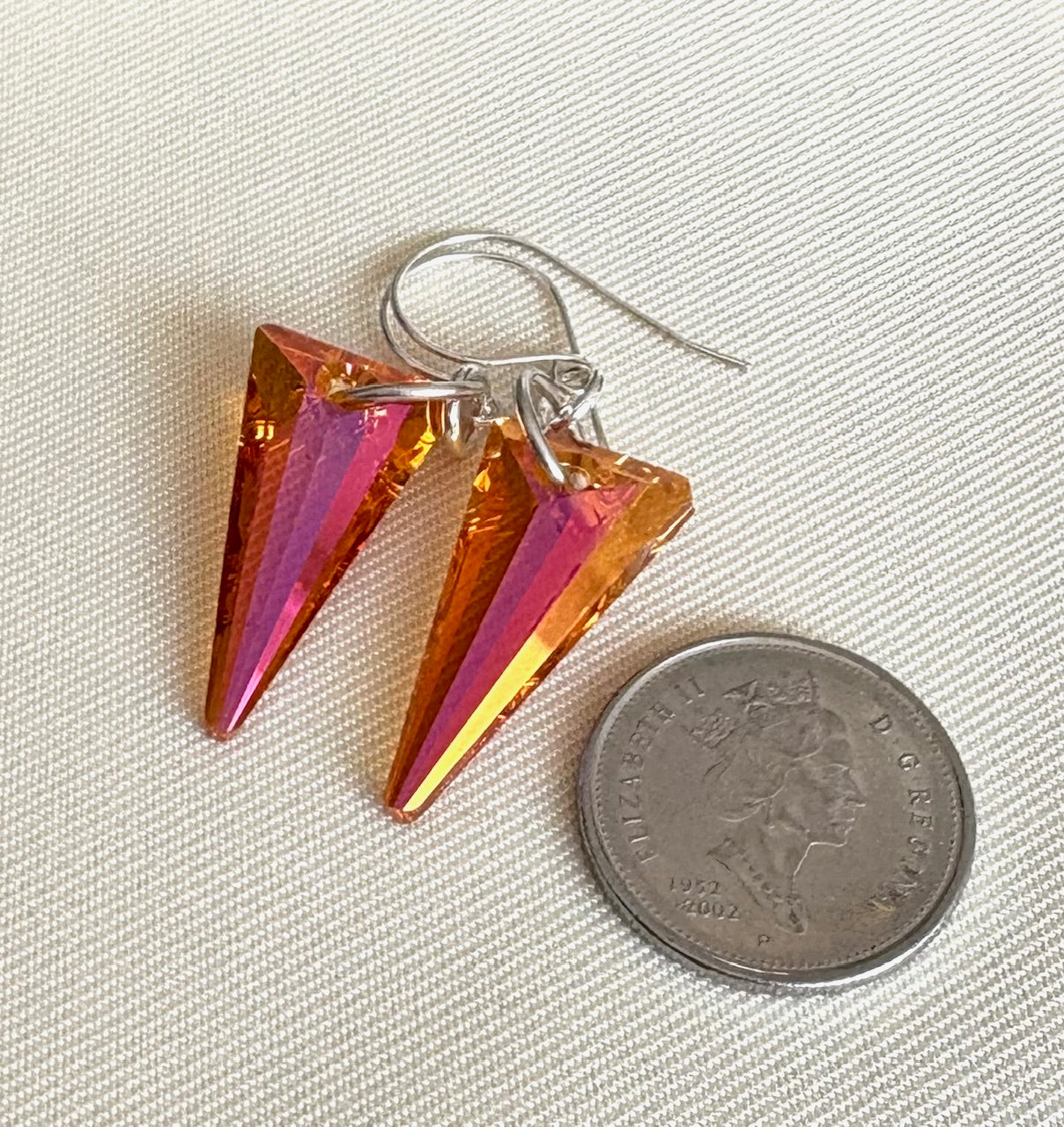 Orange spear shaped crystal drop sterling silver earrings with a coin for scale on a beige fabric background