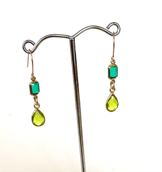 Gold earrings with green and chartruese gemstones on a stand against a white background