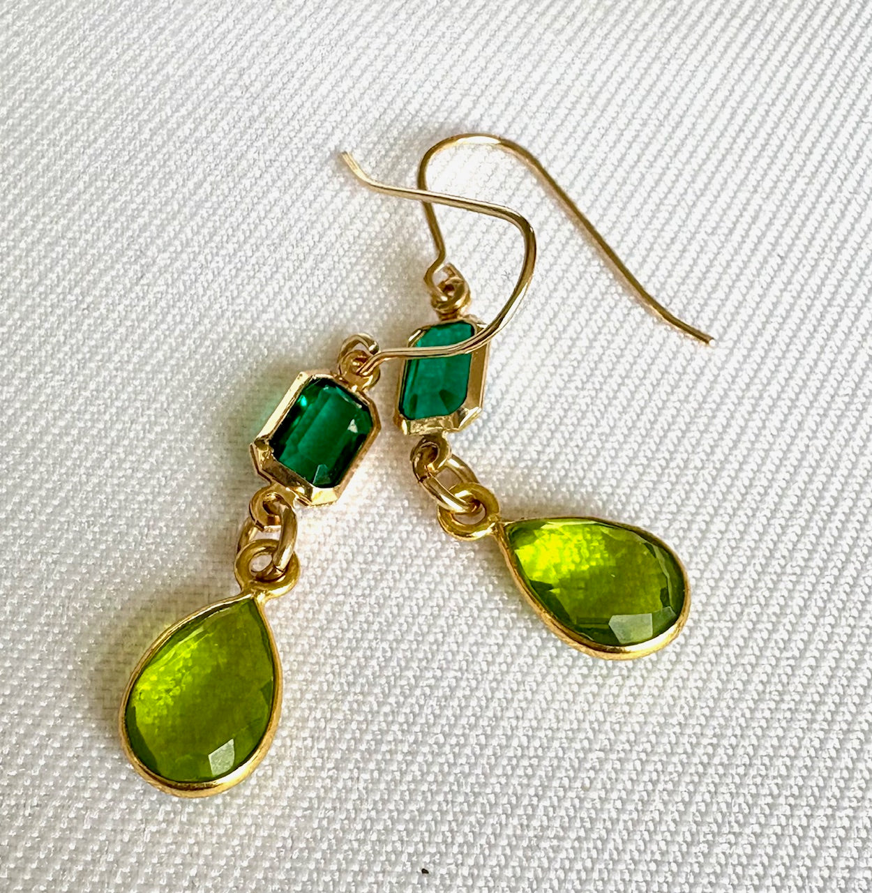 Gold earrings with green teardrop-shaped gemstones on a white background