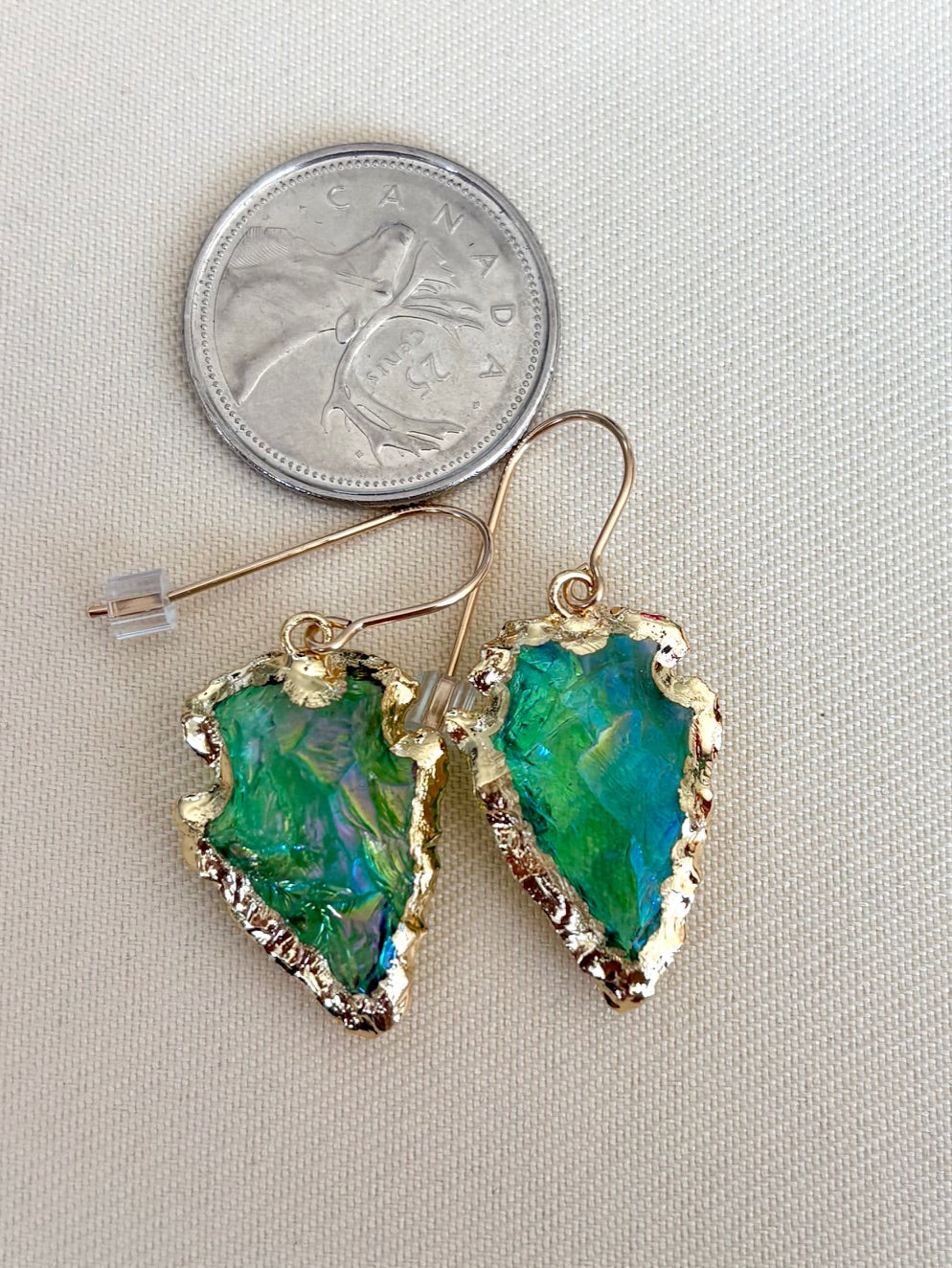 Green leaf-shaped earrings with gold accents next to a quarter for scale on a light gray background