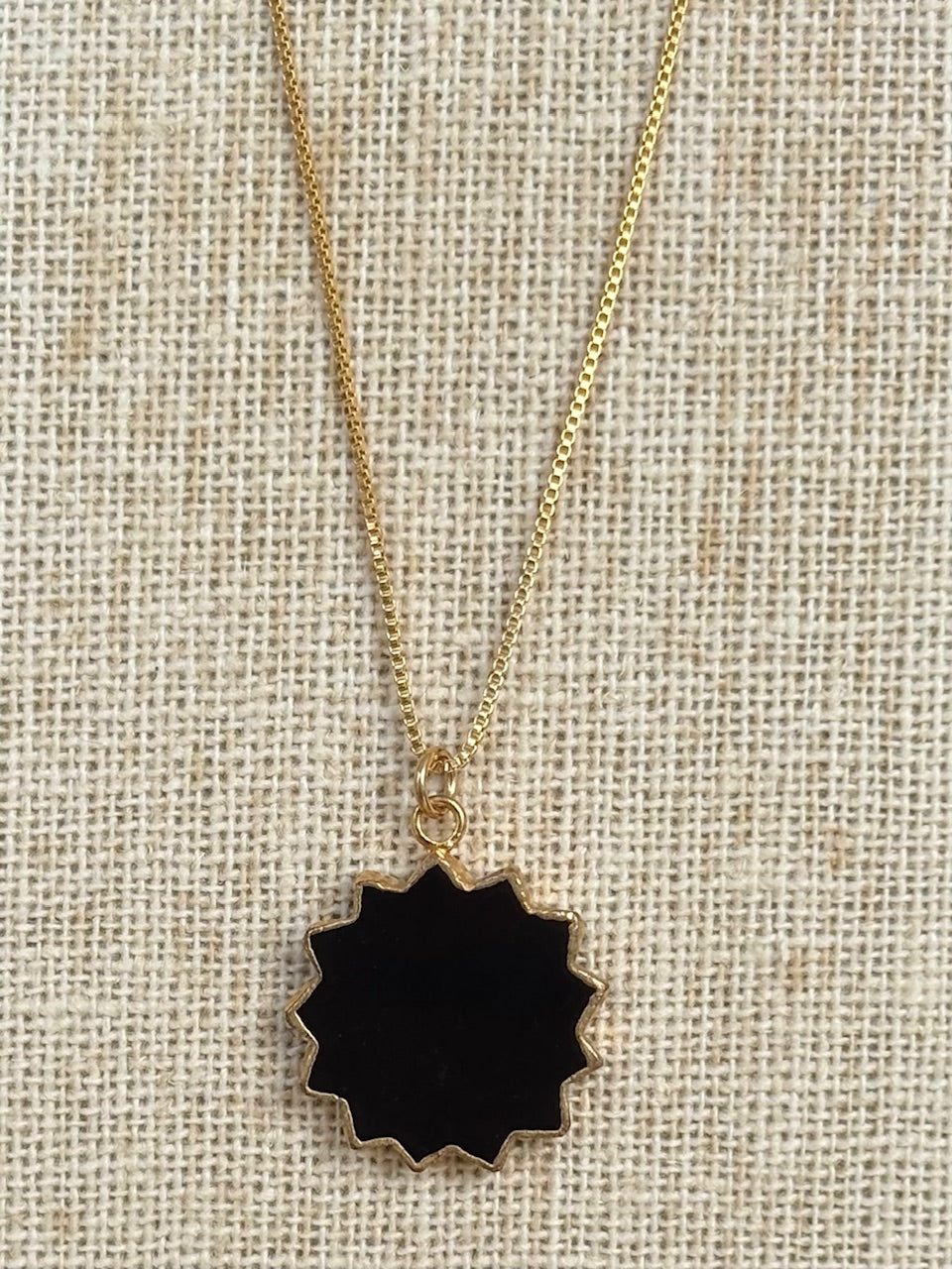 Necklace with a black sunburst pendant on a beige fabric background