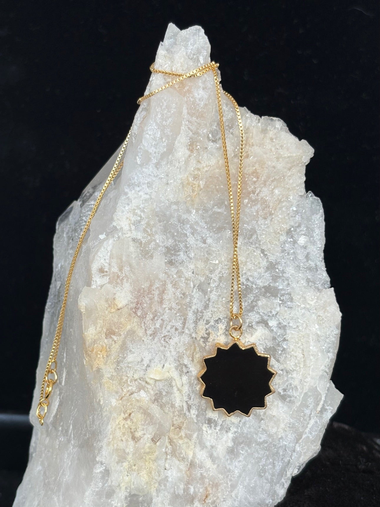 Gold necklace with a black pendant on a crystal rock against a dark background