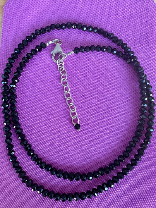 Black spinel beaded necklace with silver clasp on a purple background