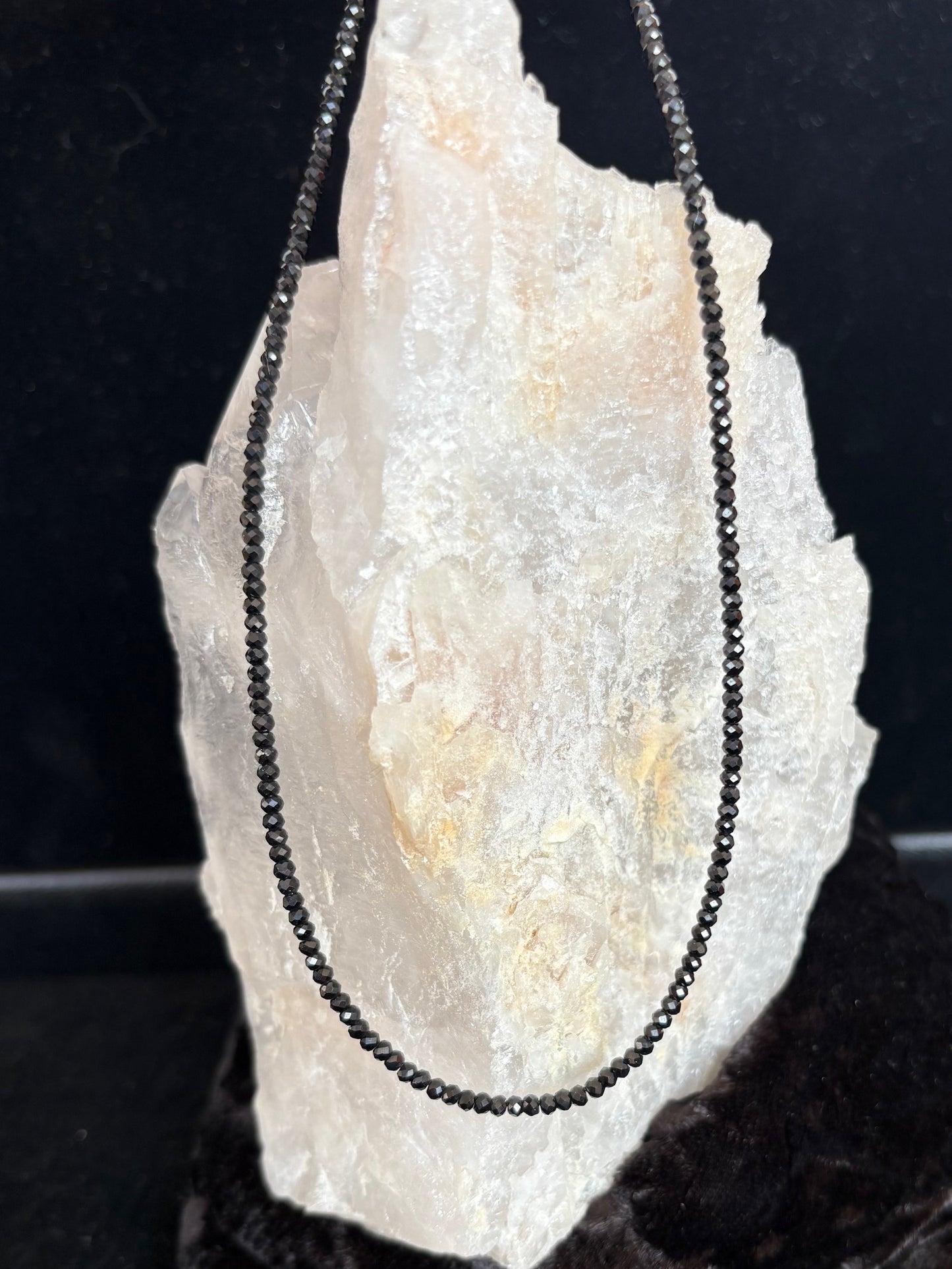 Black beaded spinel necklace on a large crystal with a dark background