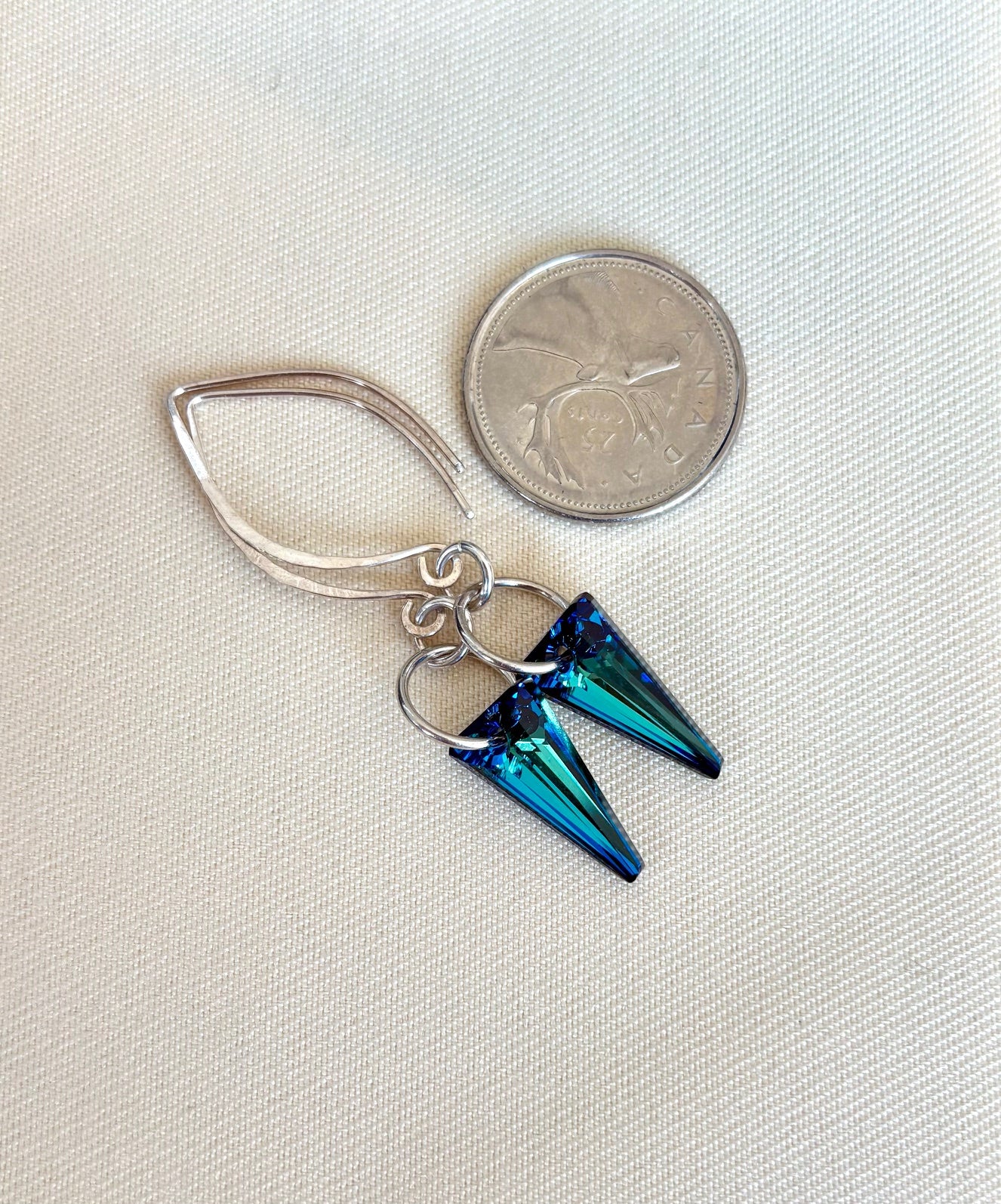 Blue spike earrings with a coin for scale on a light fabric background