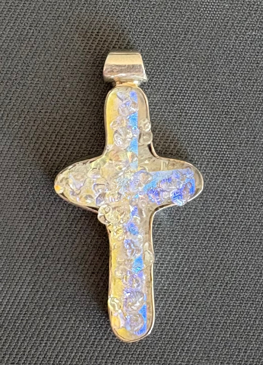 Cross-shaped pendant with iridescent finish on a gray background