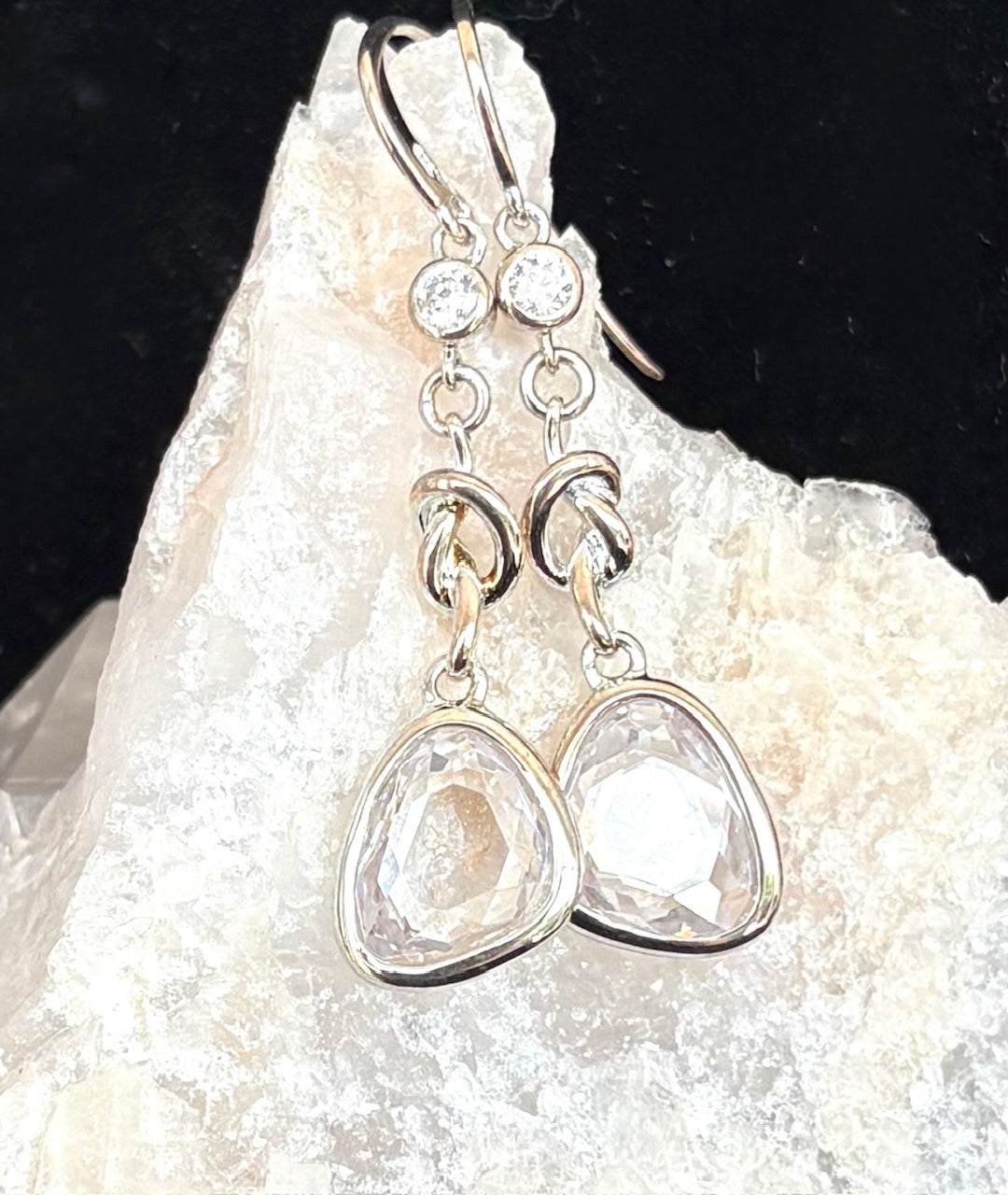 Sterling silver earrings with teardrop-shaped clear stones on a white rock background