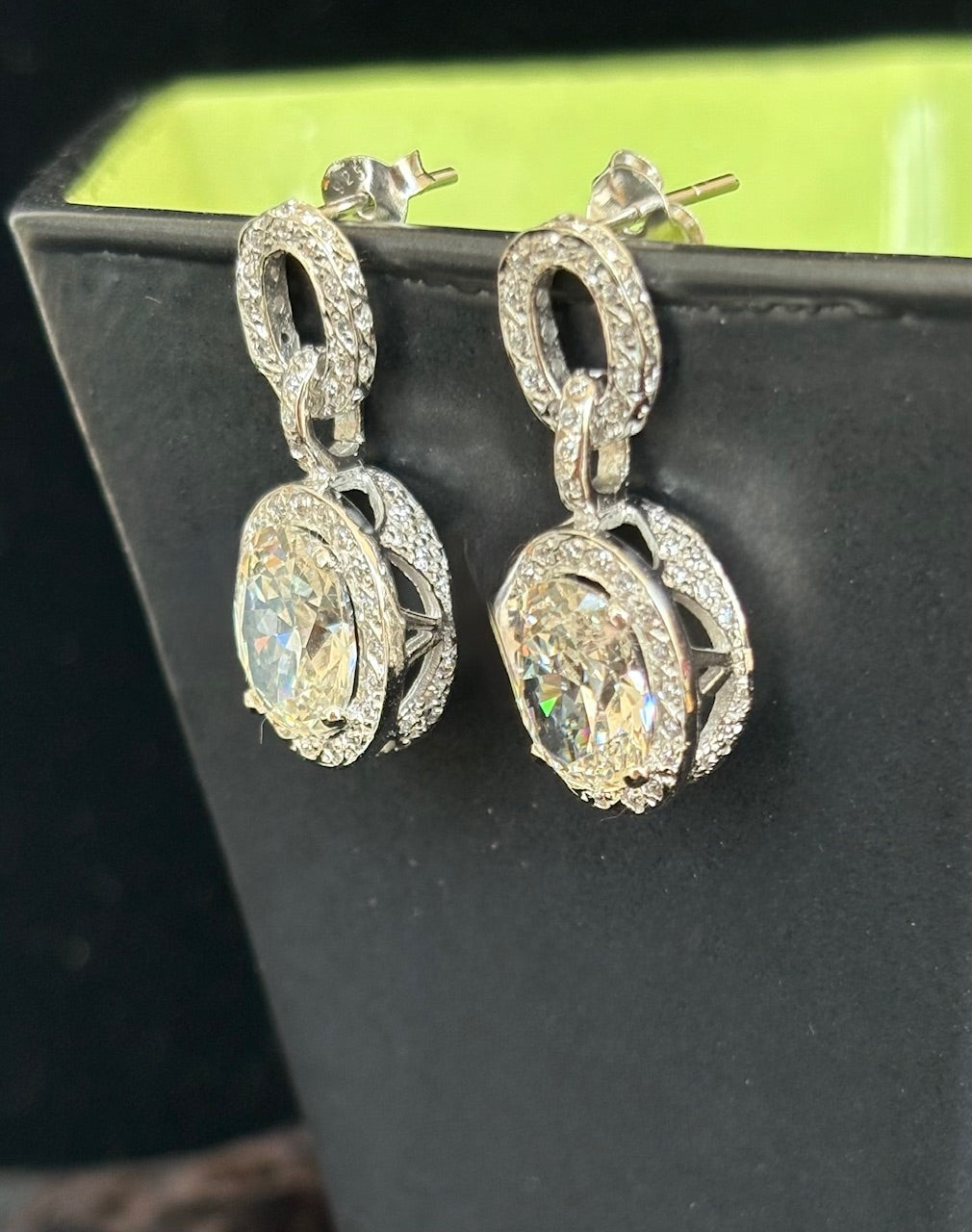 Pair of silver earrings with large gemstones on a black stand.