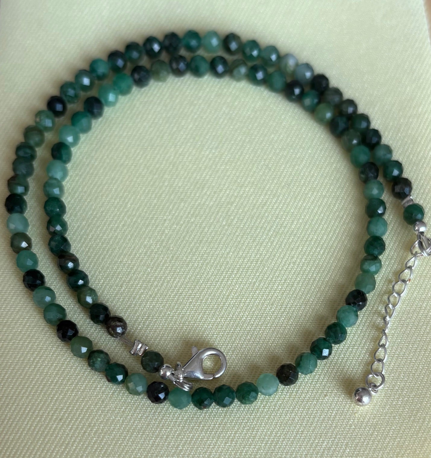Necklace with emerald gemstones on a light green fabric background
