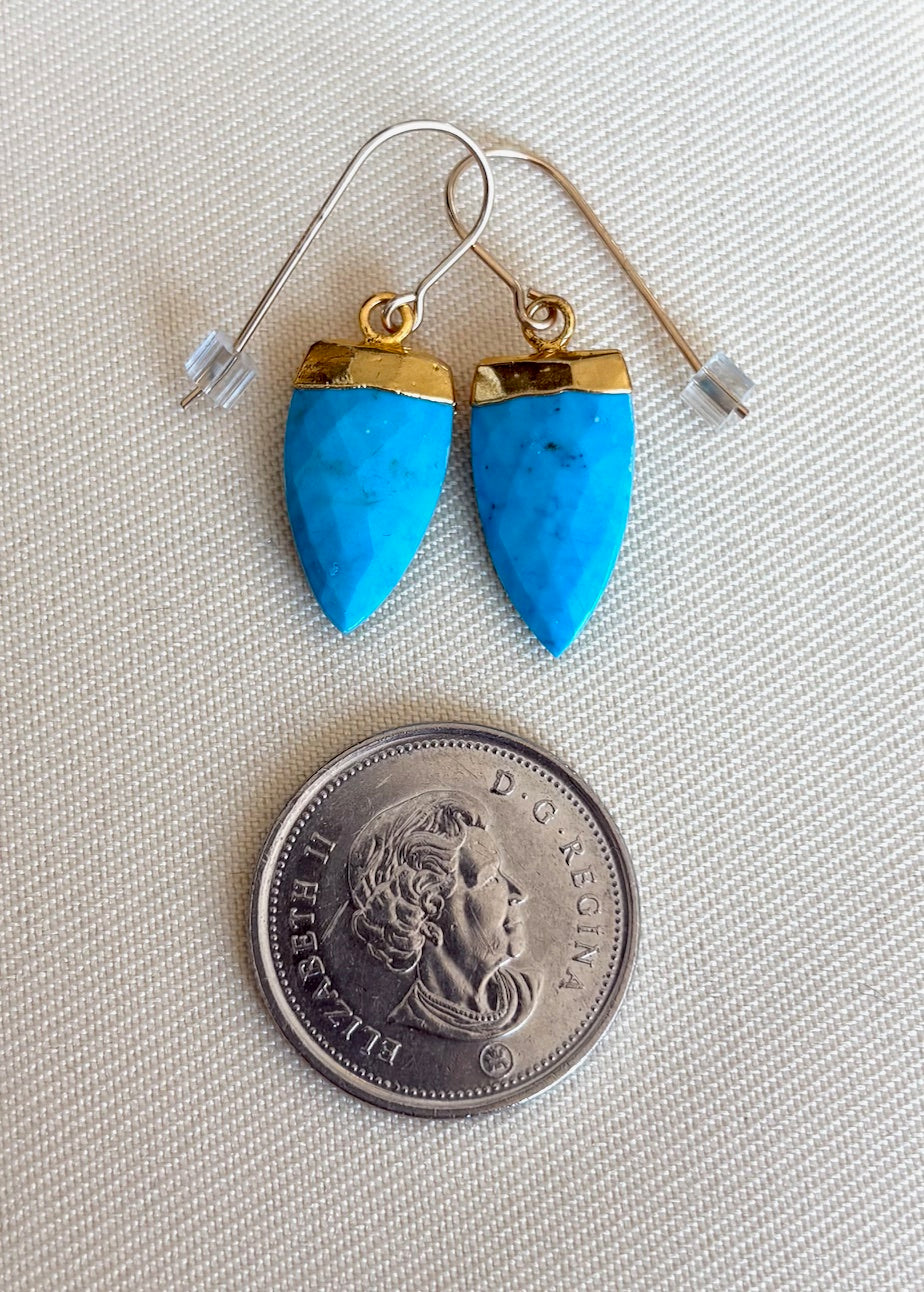 Turquoise earrings with gold accents on a coin for scale
