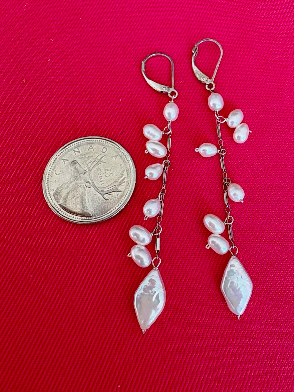 Pearl drop earrings next to a quarter on a pink background