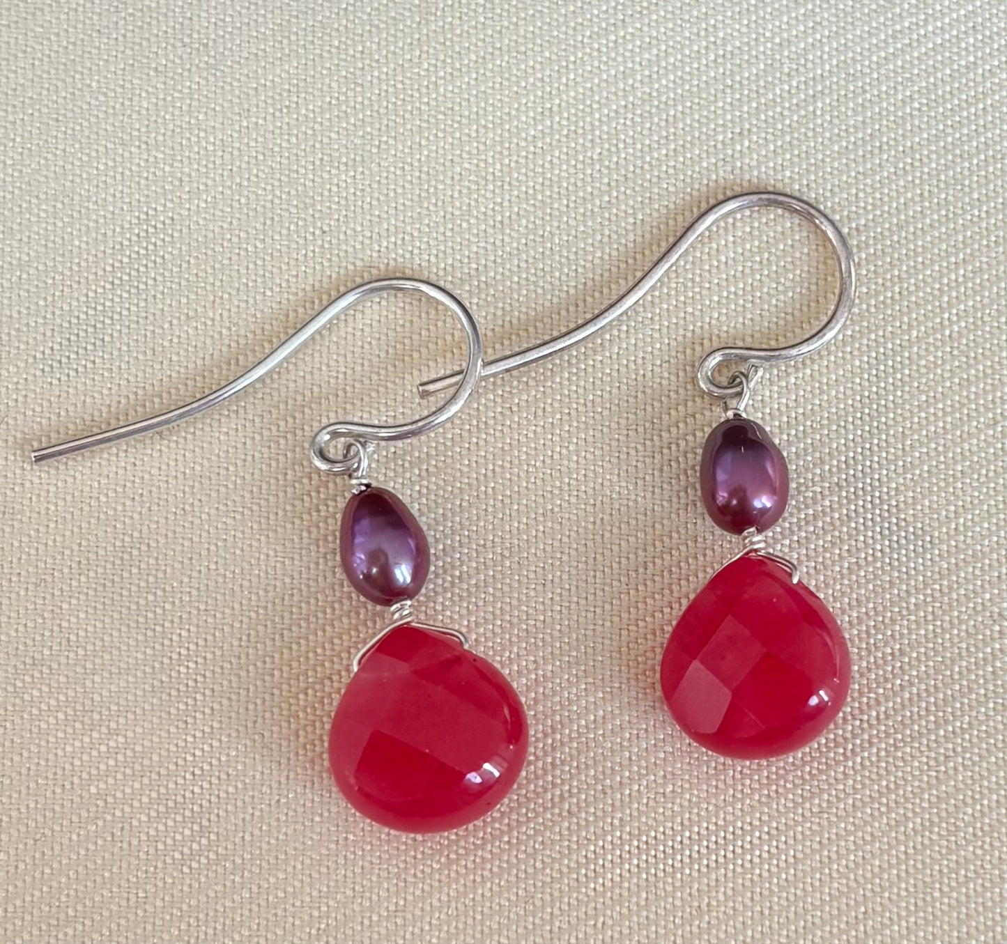 Pair of earrings with fuchsia teardrop gemstones and purple pearls on a beige background