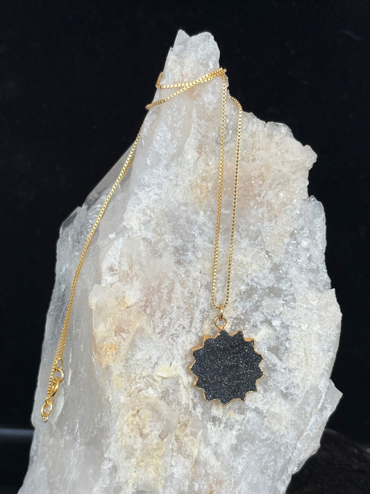 Gold necklace with a black druzy pendant on a crystal rock against a dark background