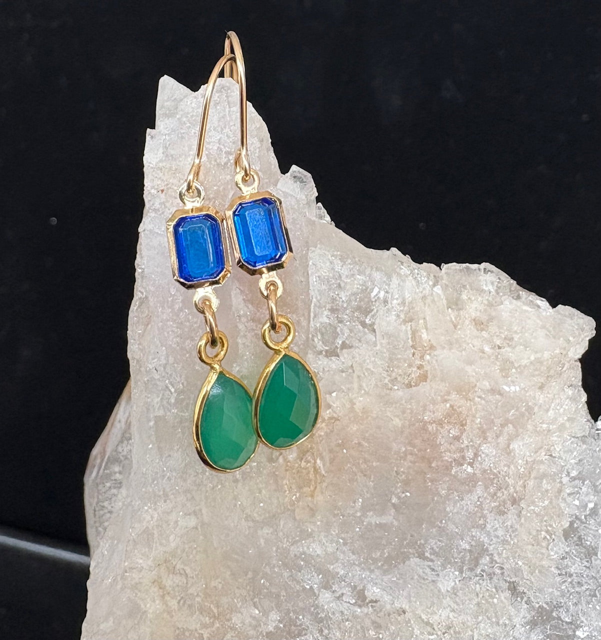 Gold earrings with blue and green stones on a crystal background