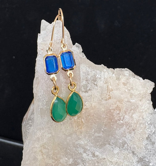 Gold earrings with blue and green stones on a crystal background
