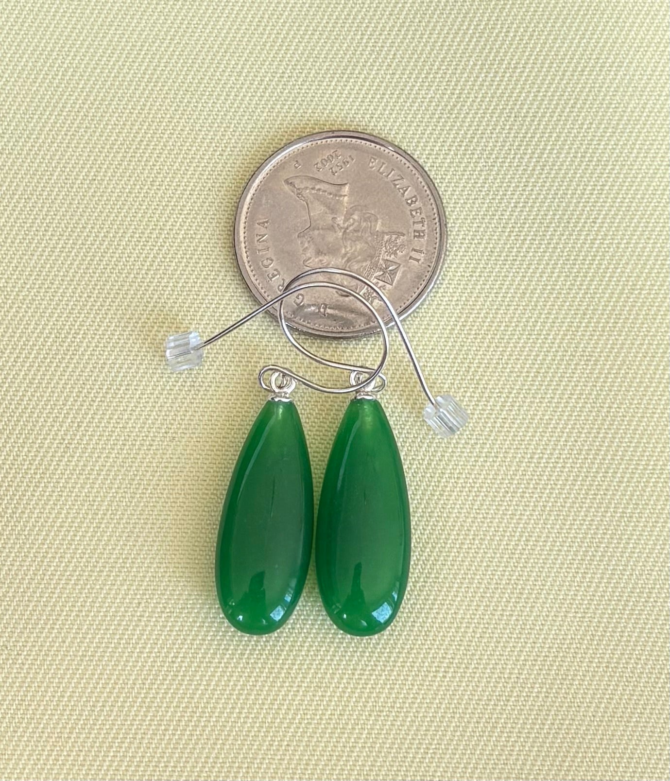 Green teardrop earrings with a quarter for scale on a beige fabric background