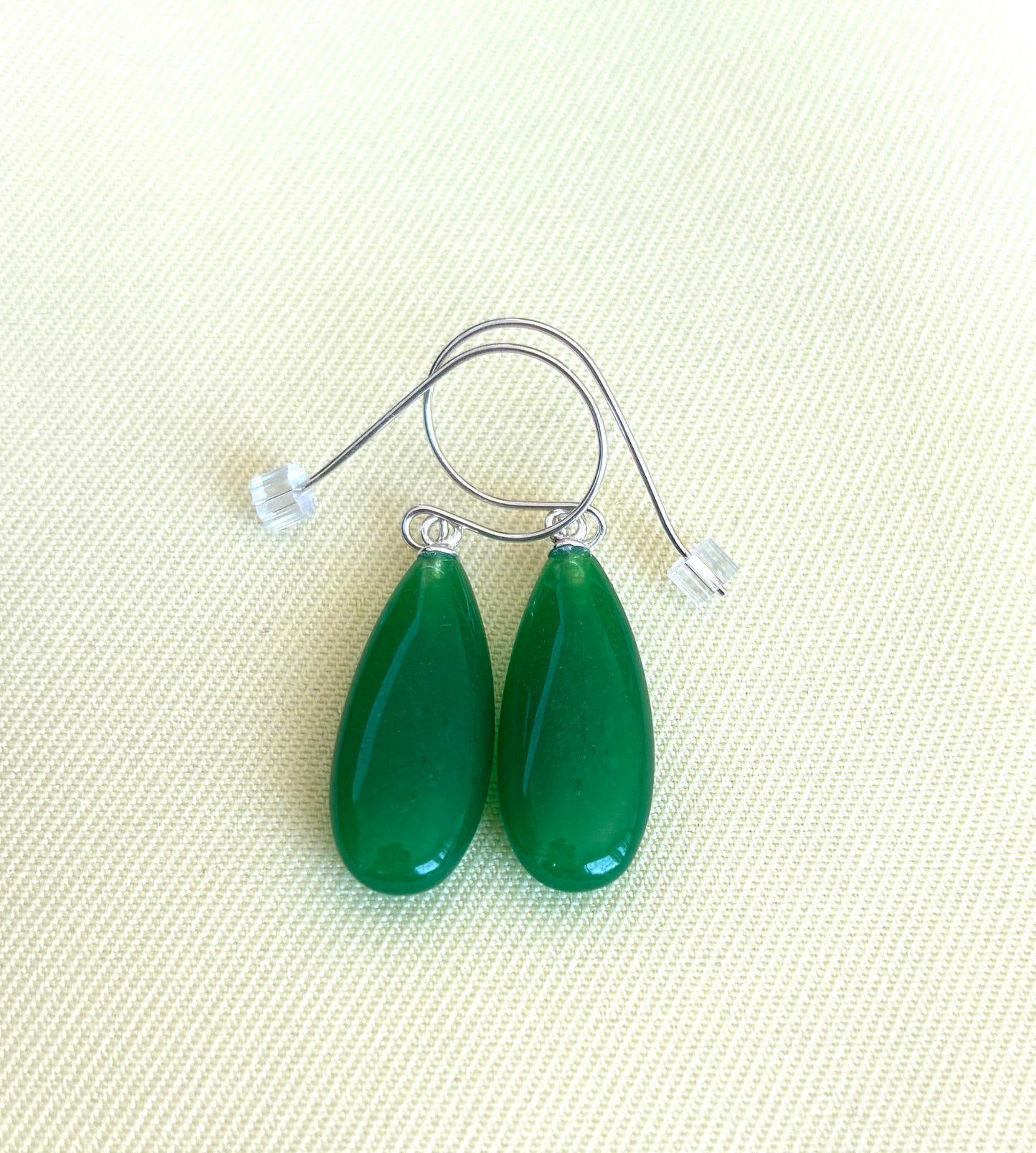 Green chalcedony teardrop earrings on a light beige fabric background