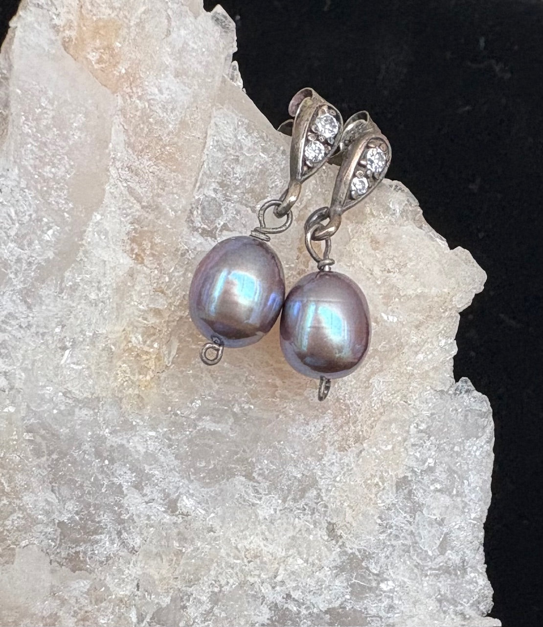 Pearl earrings with silver hooks on a textured stone background