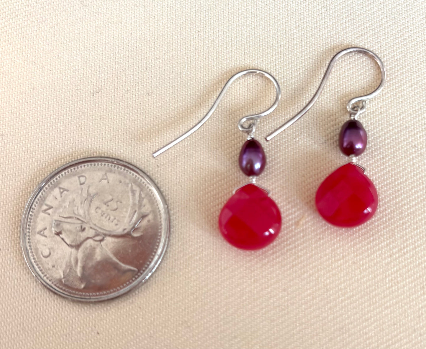 Pair of fuchsia teardrop gemstone earrings with purple pearls on silver hooks, shown next to a Canadian quarter for scale.