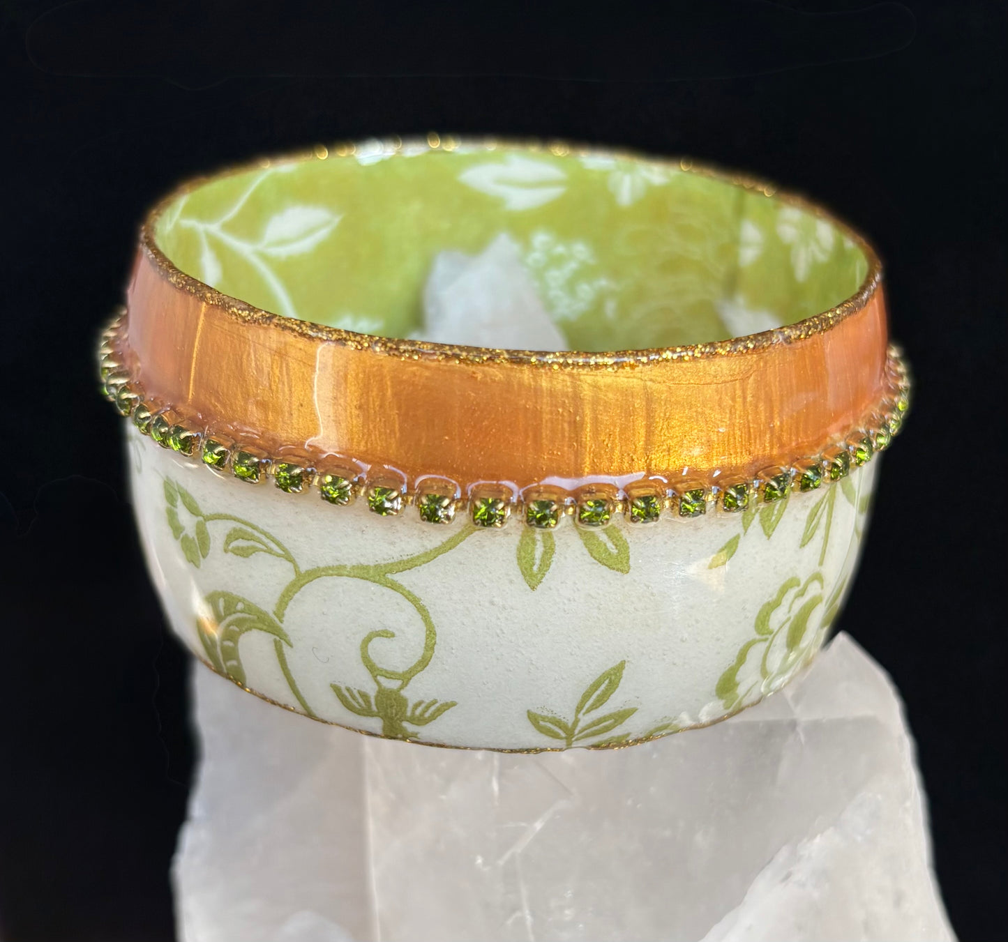 Decorative bracelet bangle with gold rim and green floral patterns on a white background