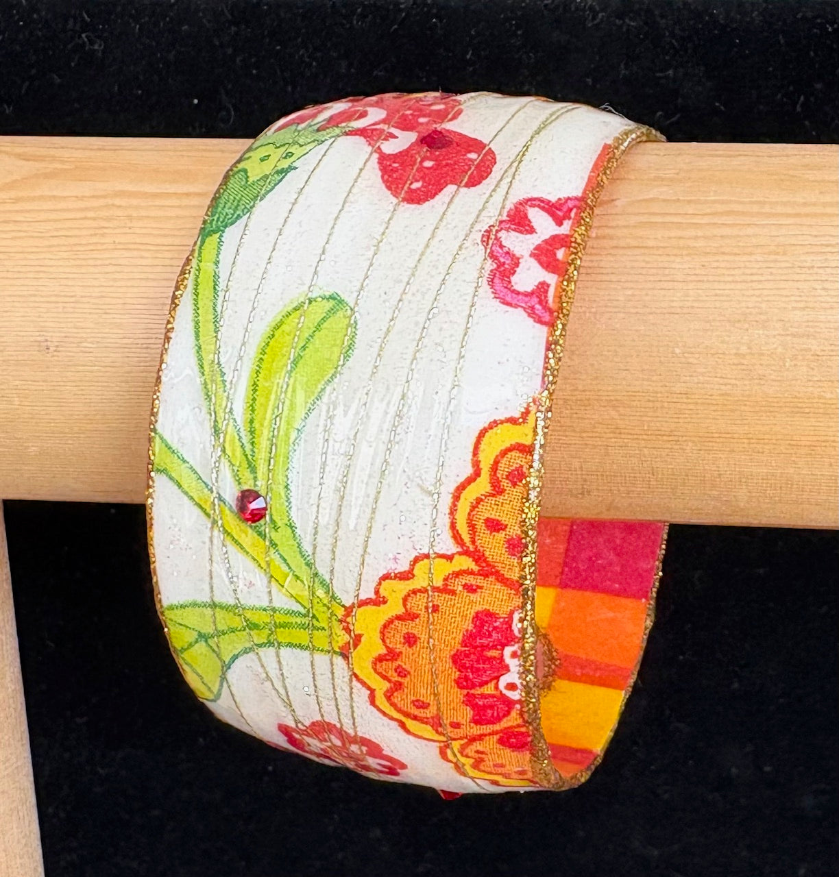 Colorful floral-patterned bracelet on a wooden display against a black background