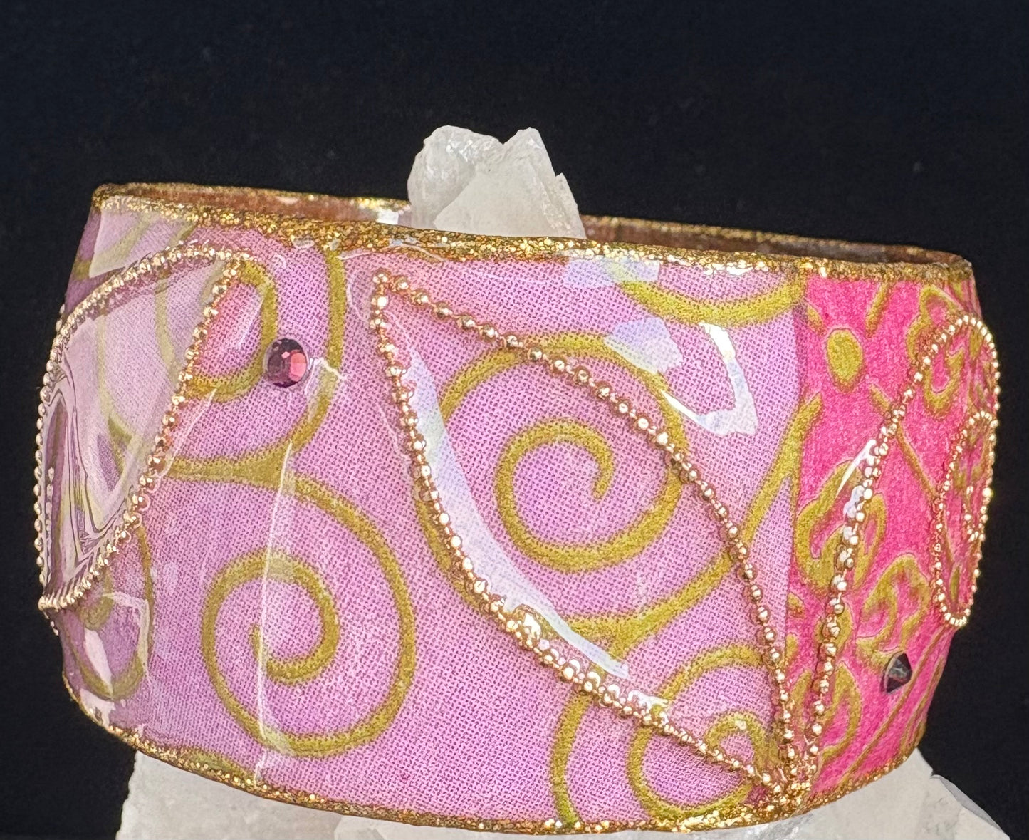 Decorative bangle with pink fabric and gold embroidery on a black background