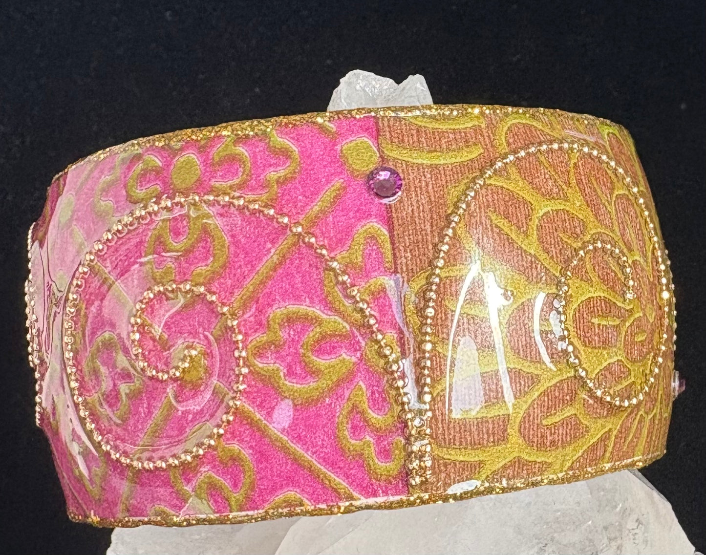 Decorative pink and gold bangle with intricate patterns on a black background