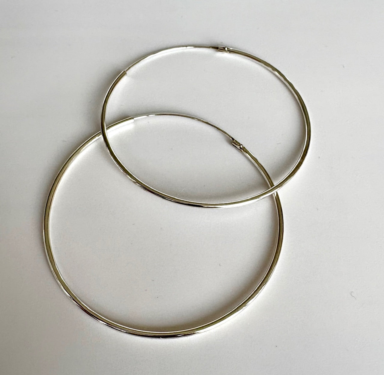 Two silver hoop earrings on a light gray background by Jolie Esprit