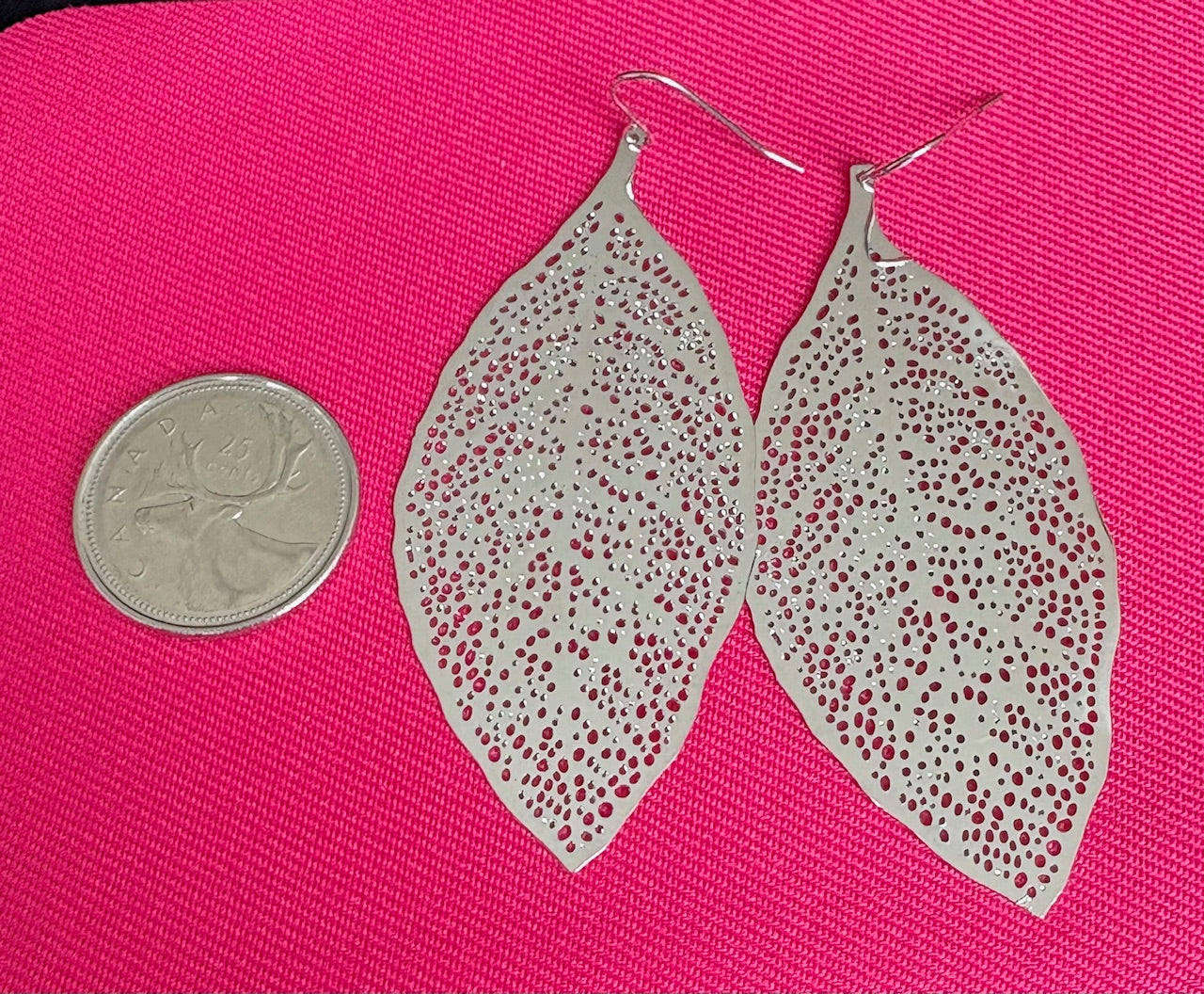 Leather leaf earrings with red speckles on a pink background, next to a coin for scale.