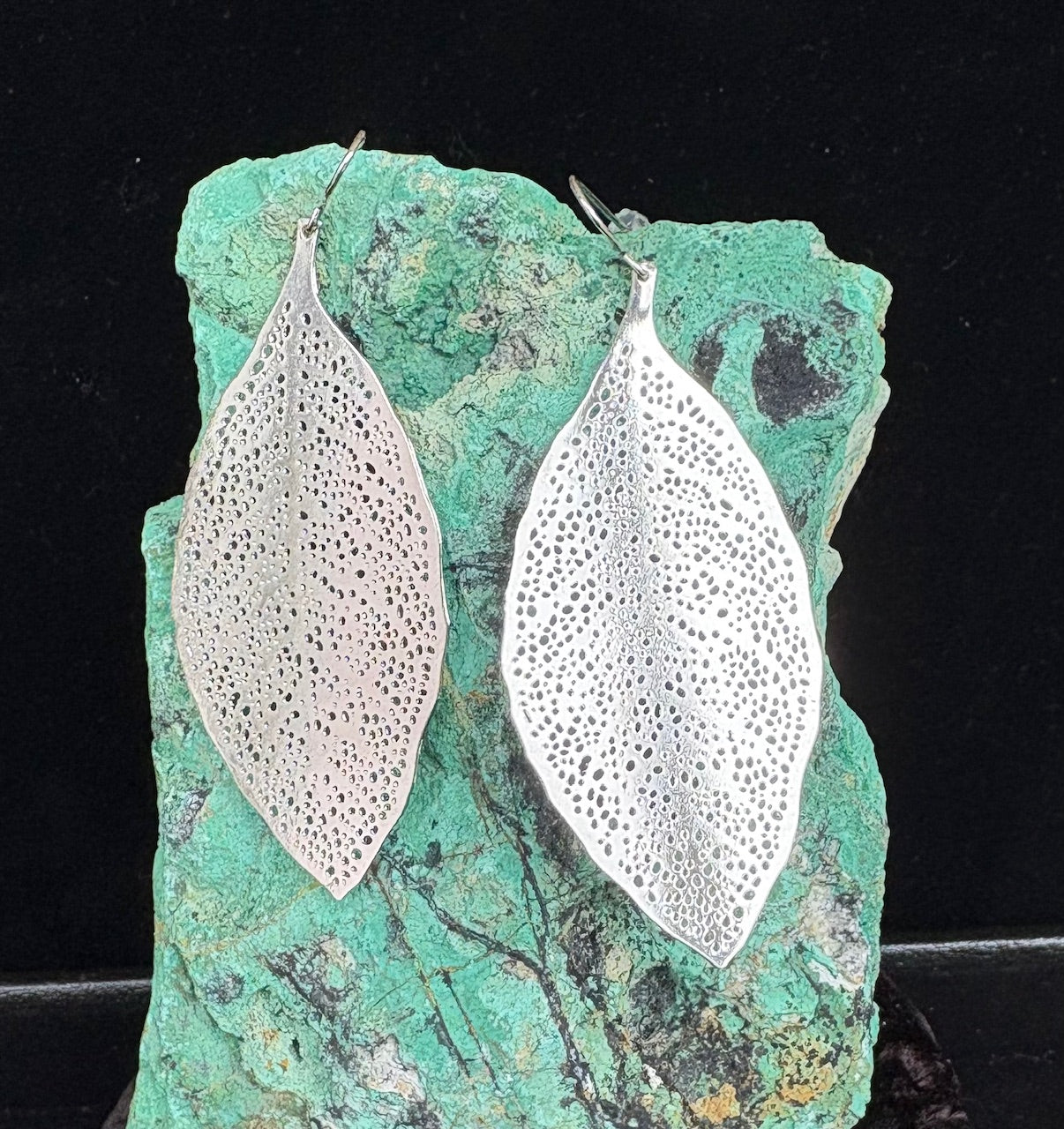 Silver leaf-shaped earrings on a green stone background