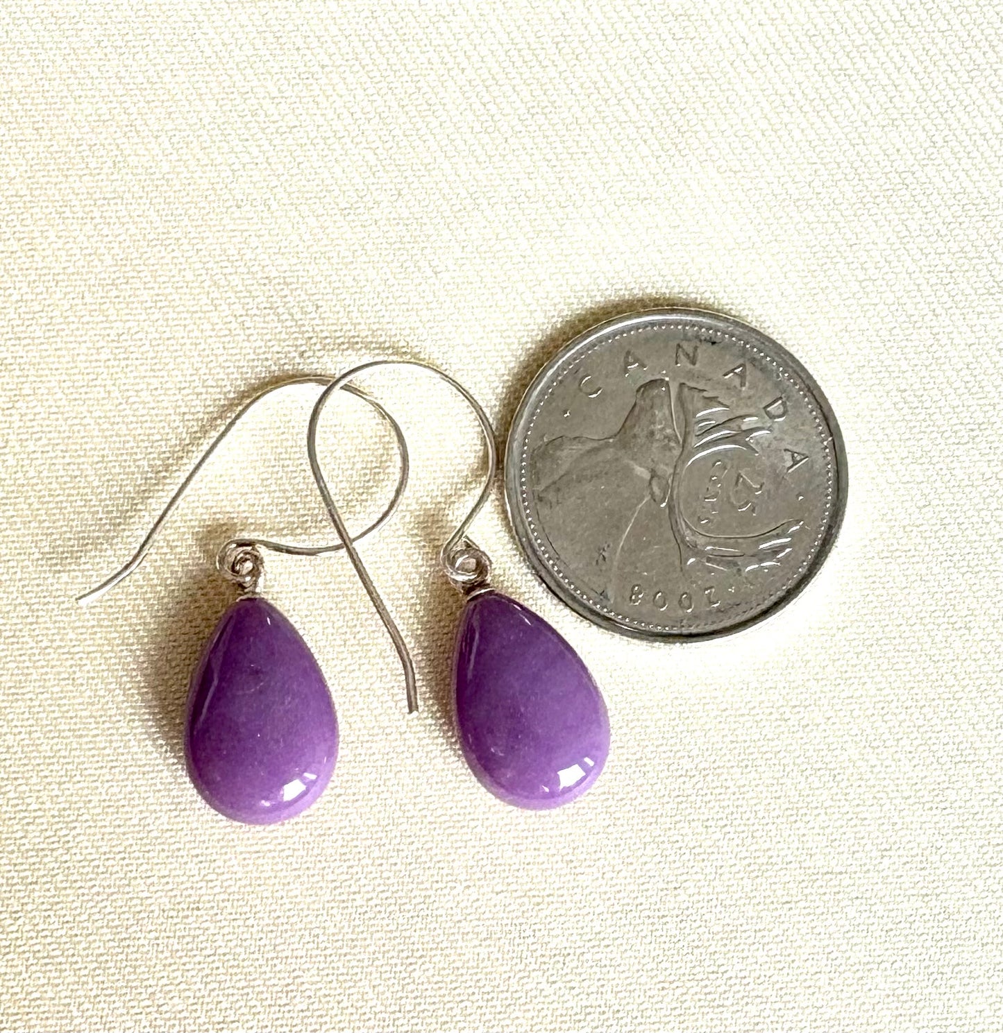 Purple teardrop earrings next to a Canadian quarter on a beige background