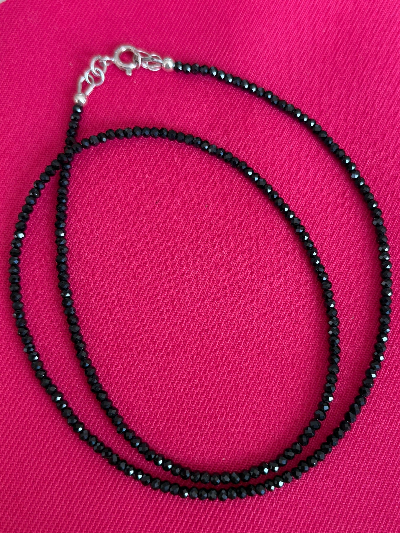 Black micro faceted spinel necklace on a pink background