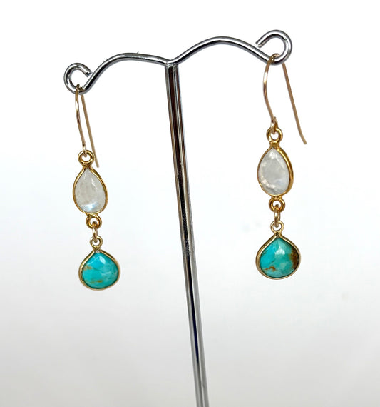 Pair of earrings with turquoise and moonstones on a stand against a white background