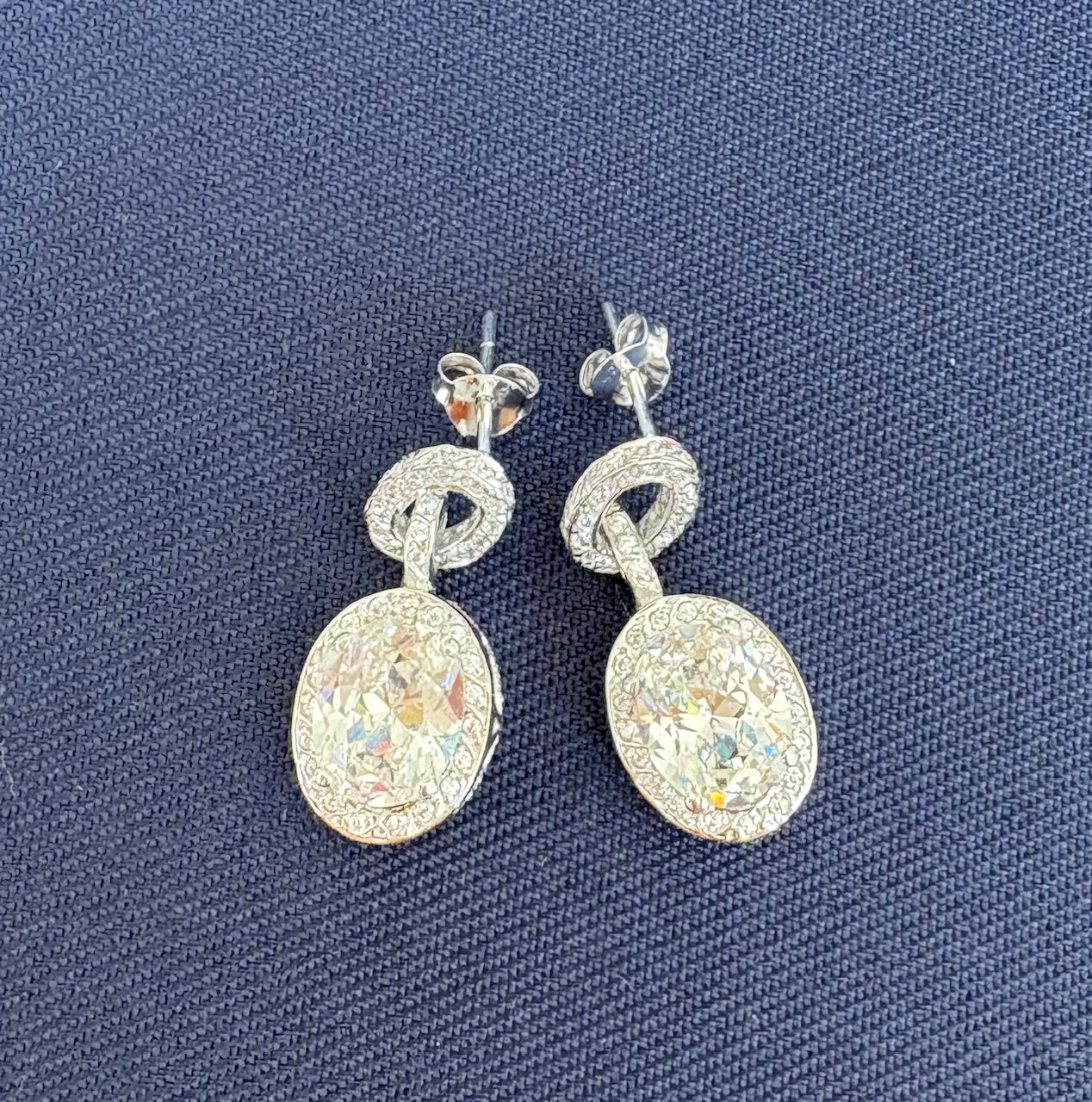 Pair of silver earrings with crystal like stones on a blue textured background