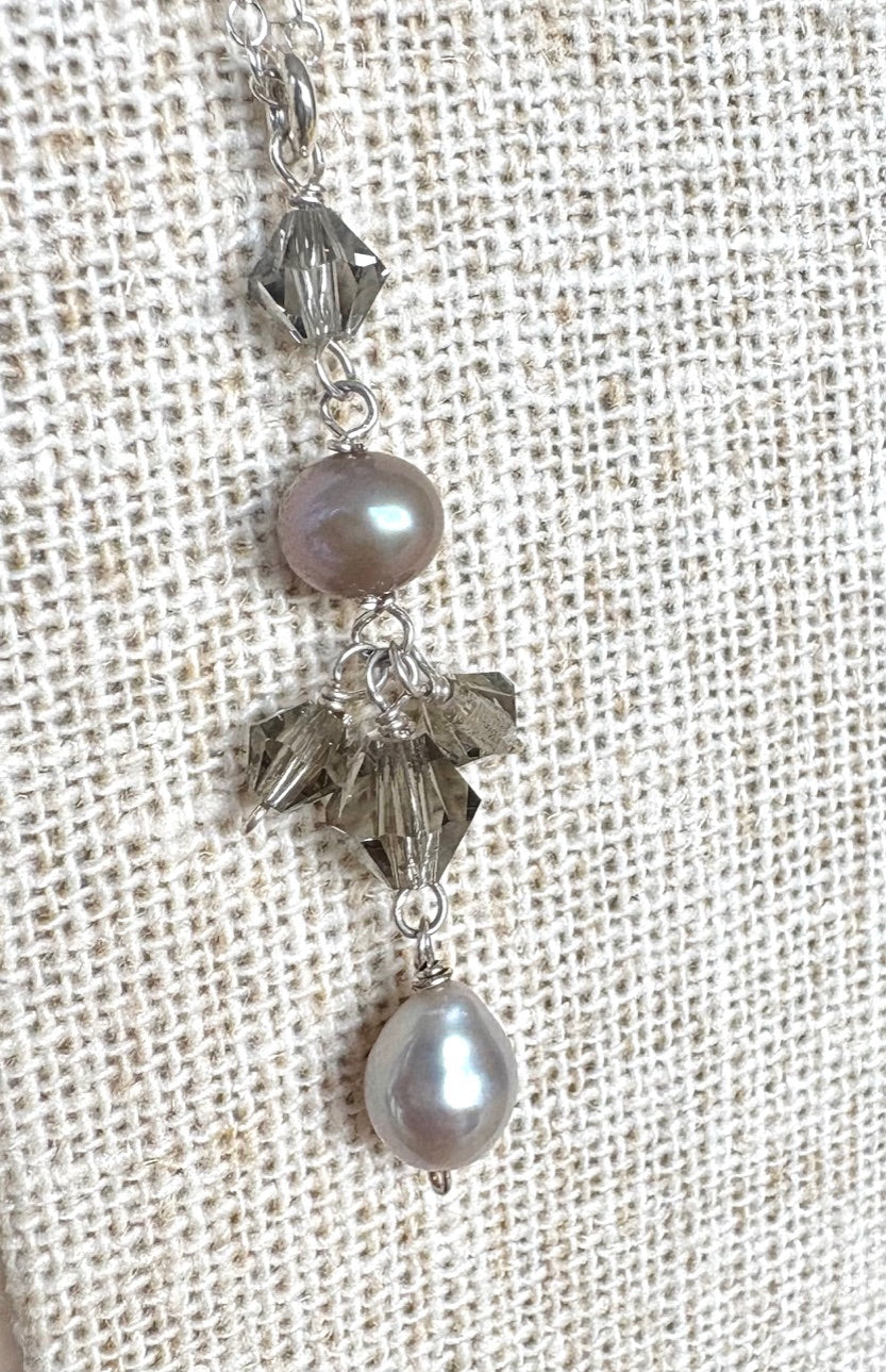 Necklace with gray pearls and swarvoski pendant on a textured beige background