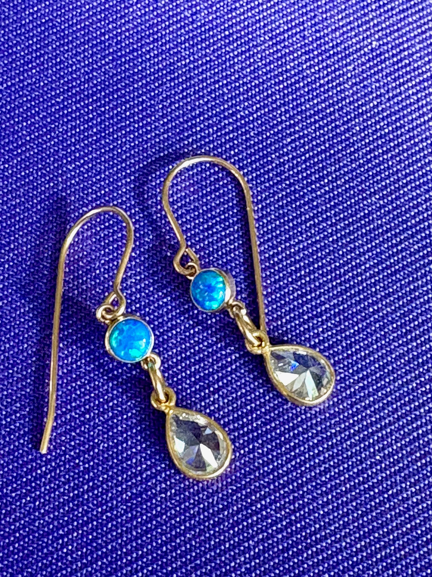 Gold earrings with opal gemstones on a blue fabric background