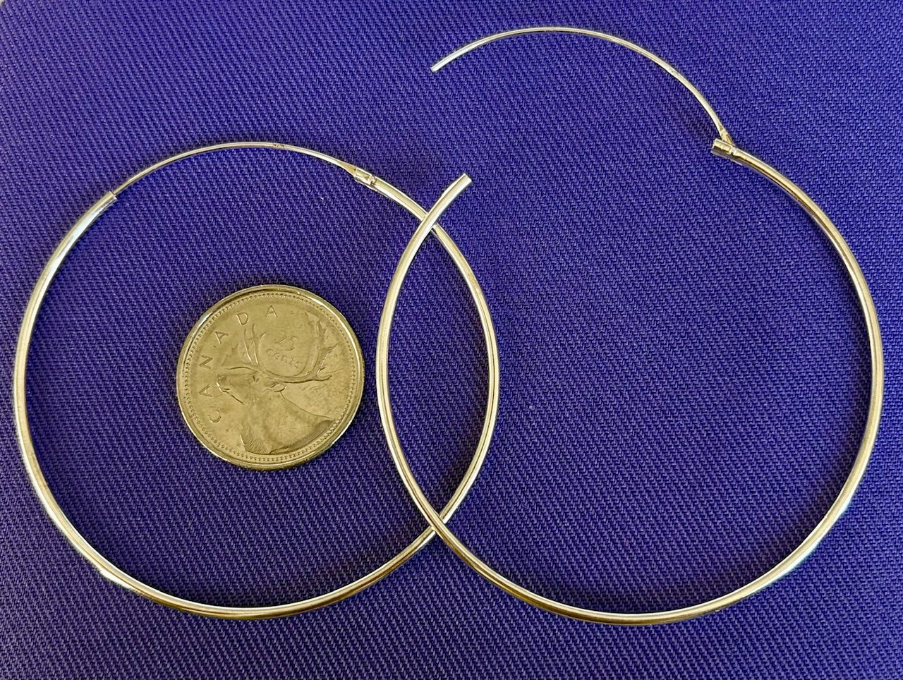 Two sterling silver hoop earrings on a blue fabric background with a coin for scale.