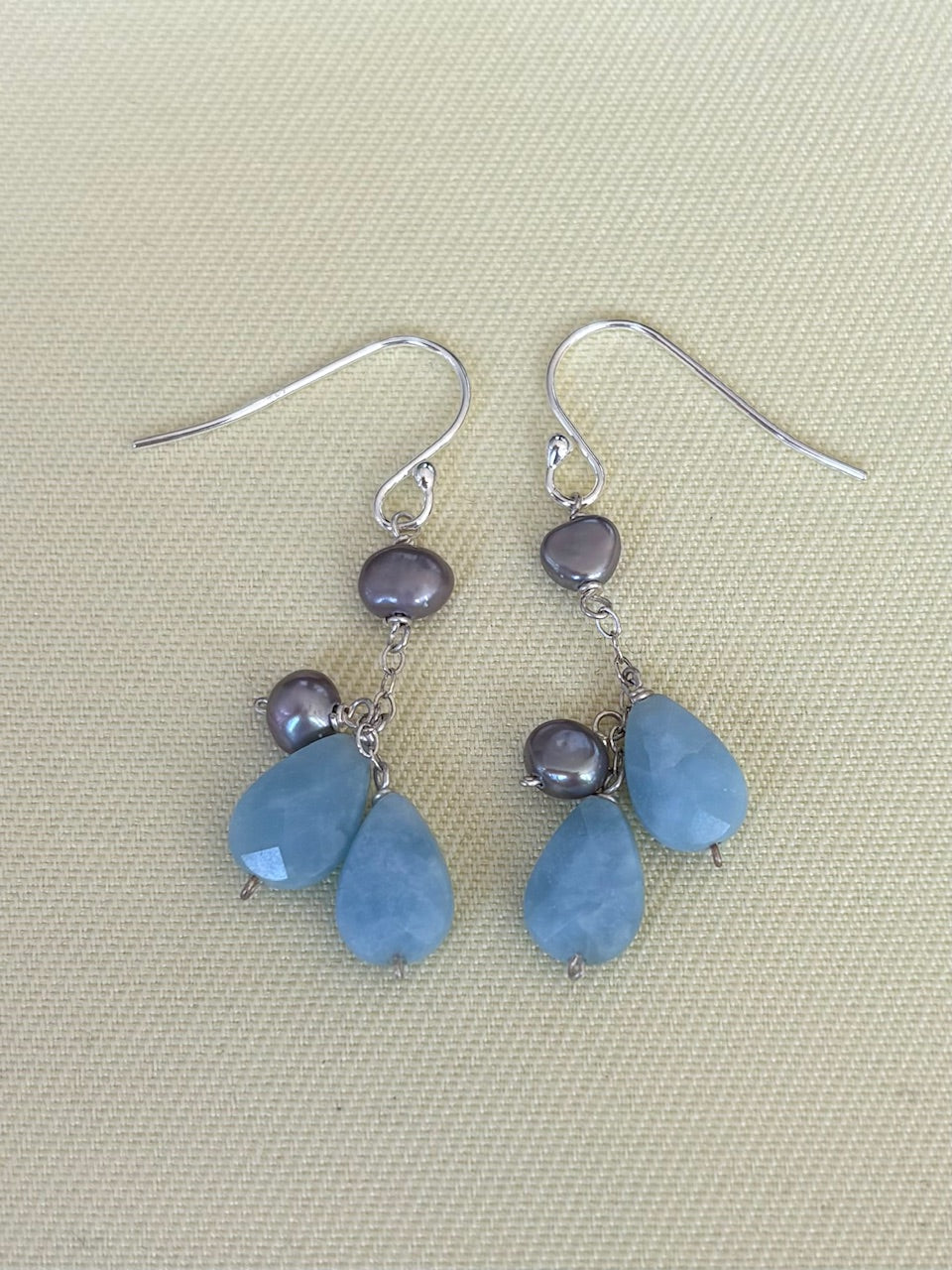 Pair of earrings with blue teardrop-shaped amazonite stones and pearls on a beige fabric background