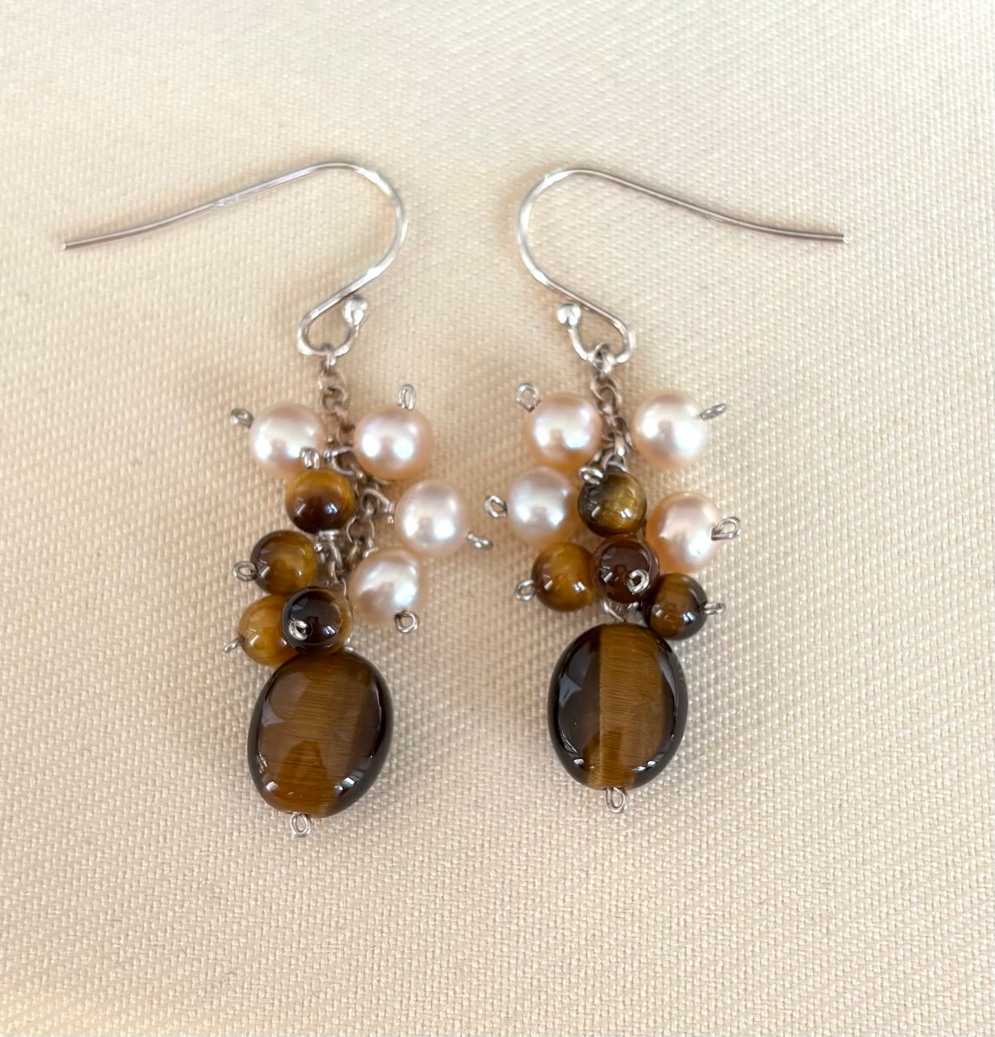 Pair of earrings with Tigers Eye stones and pearls on a beige background