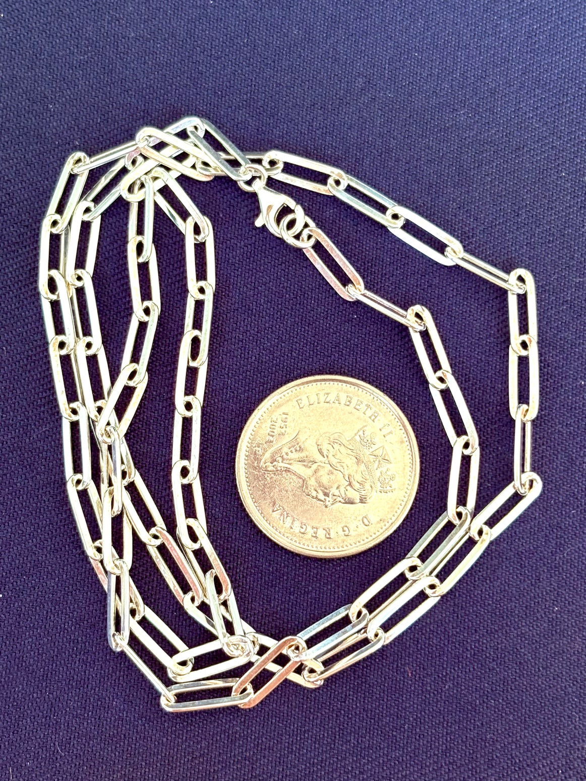 Silver chain necklace on a purple background with a coin for scale