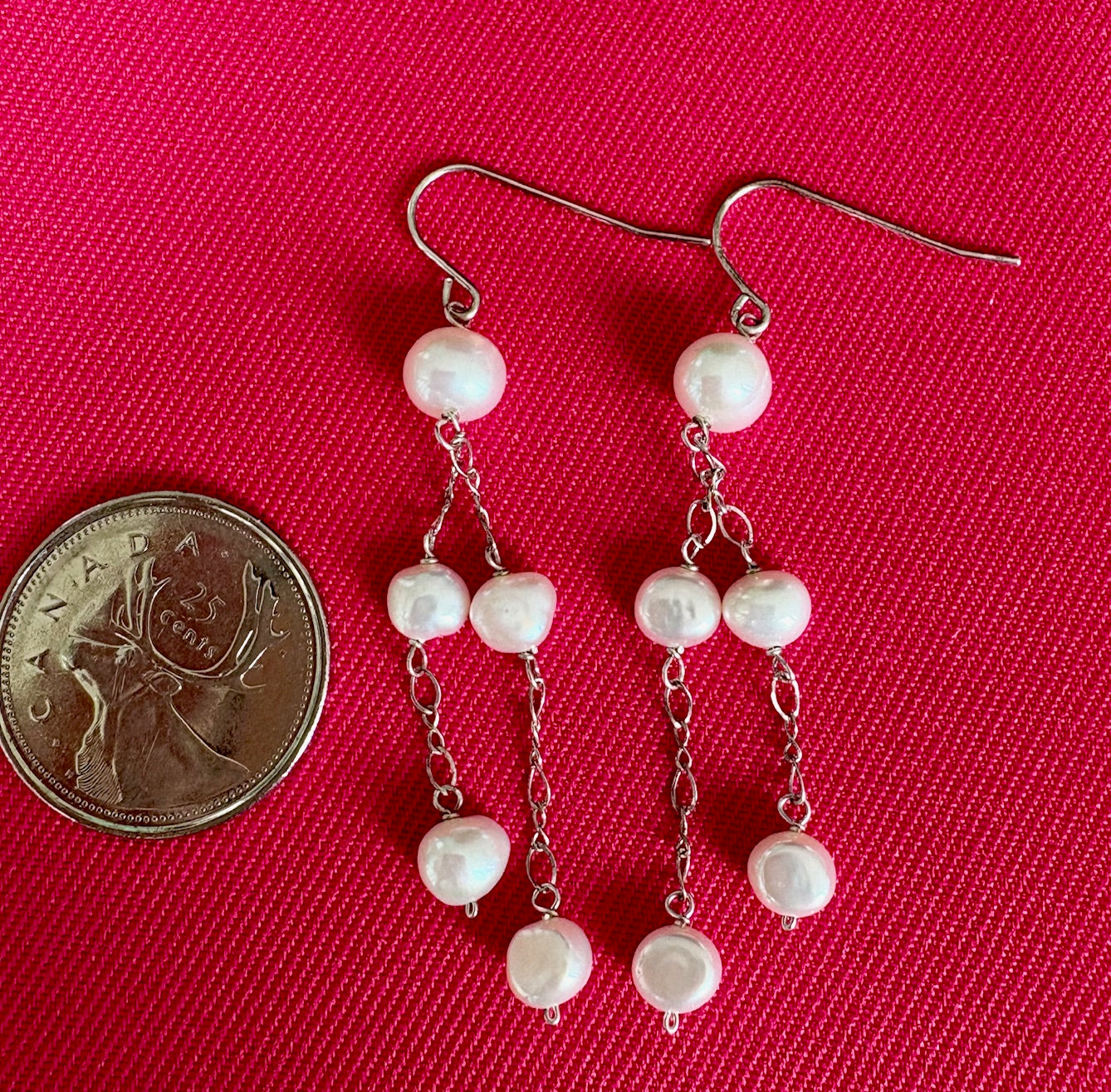 Jolie Esprit pearl earrings with a coin for scale on a pink background