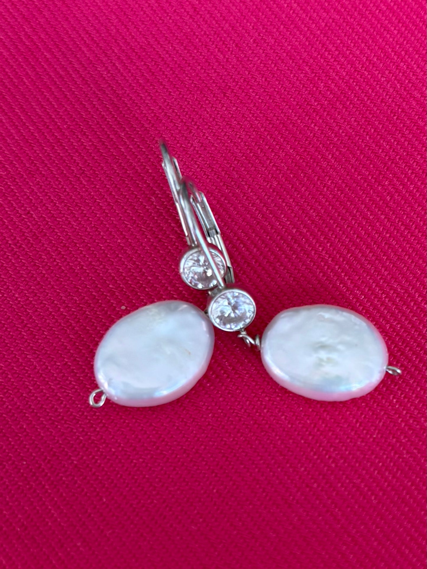 Pearl earrings with silver hooks on a pink fabric background