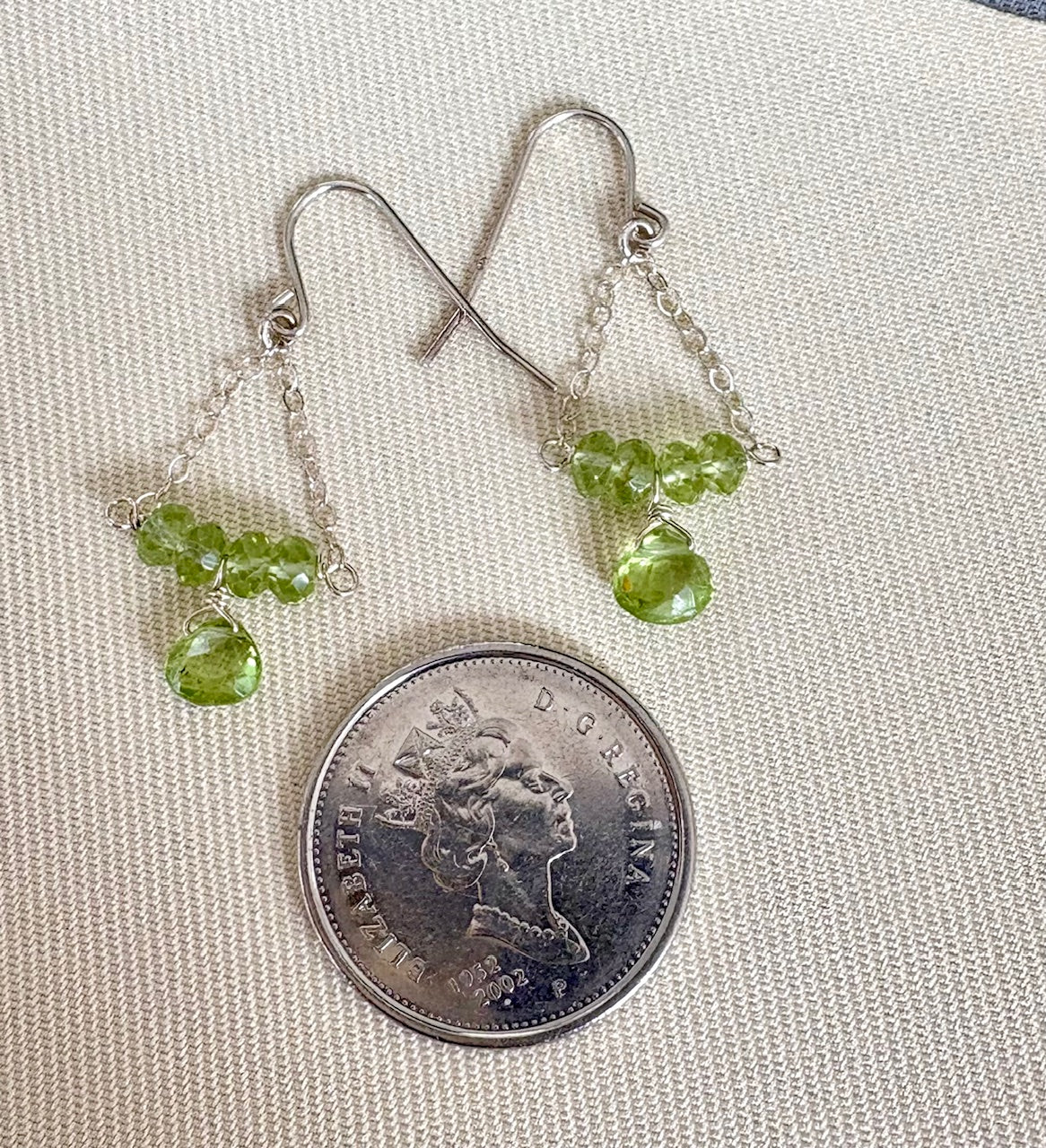 Silver earrings with green gemstones on a coin for scale
