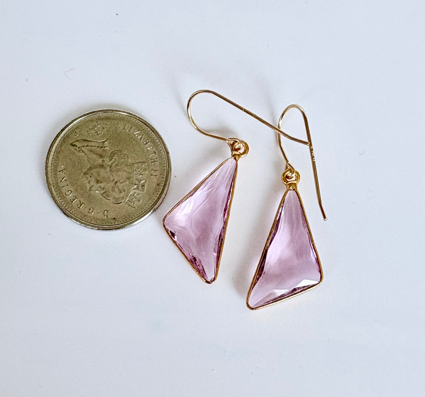 Pink triangle earrings with gold hooks on a white background, next to a coin for scale.