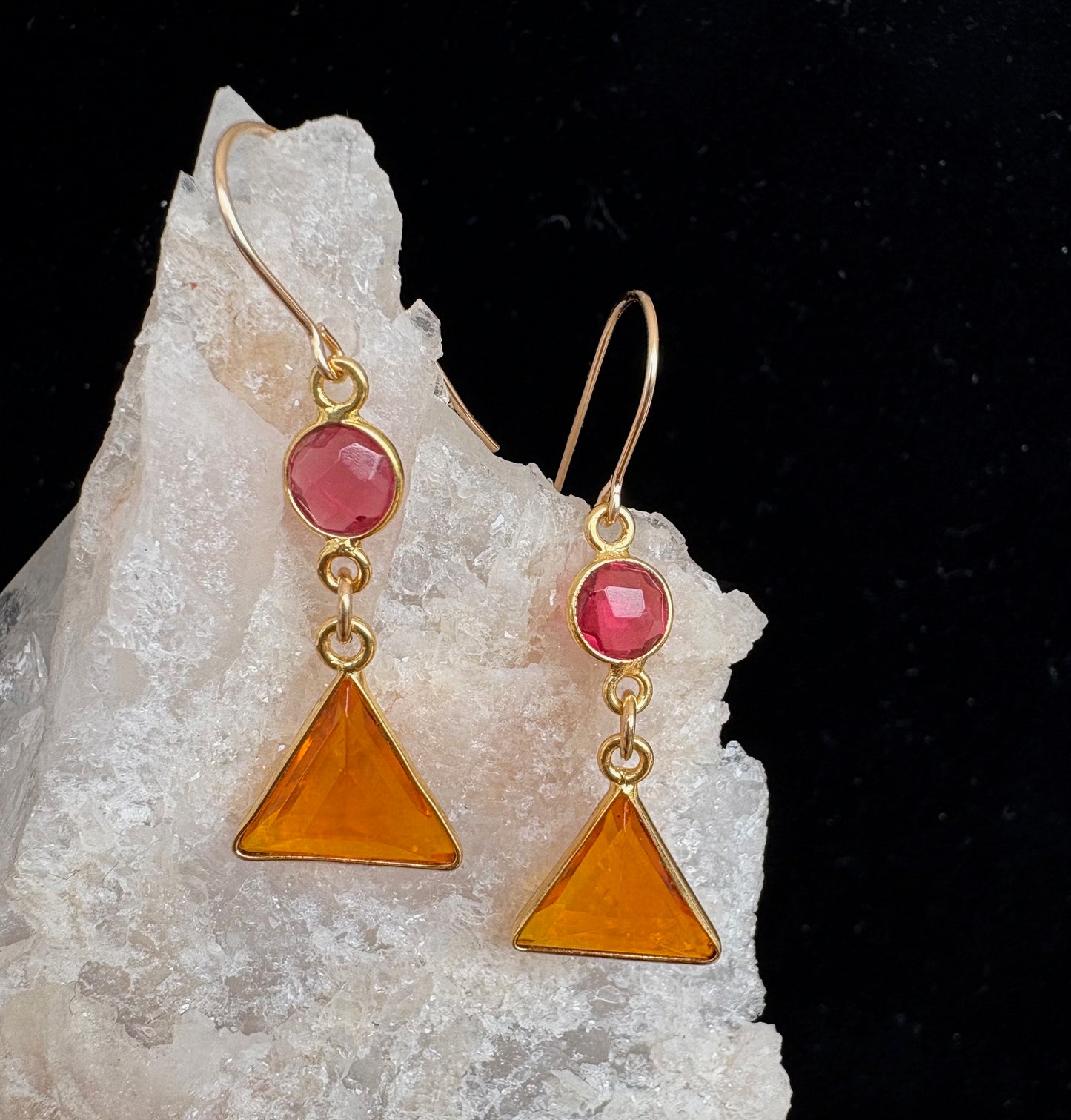 Gold earrings with pink and orange triangular stones on a crystal background