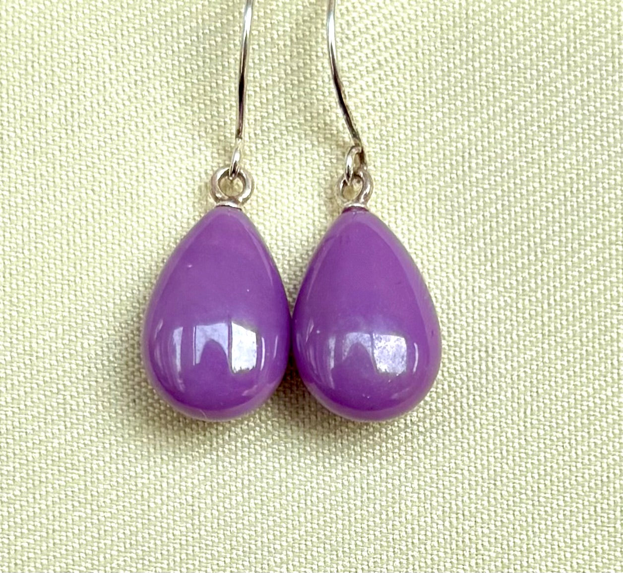 Purple teardrop earrings on a light green fabric background