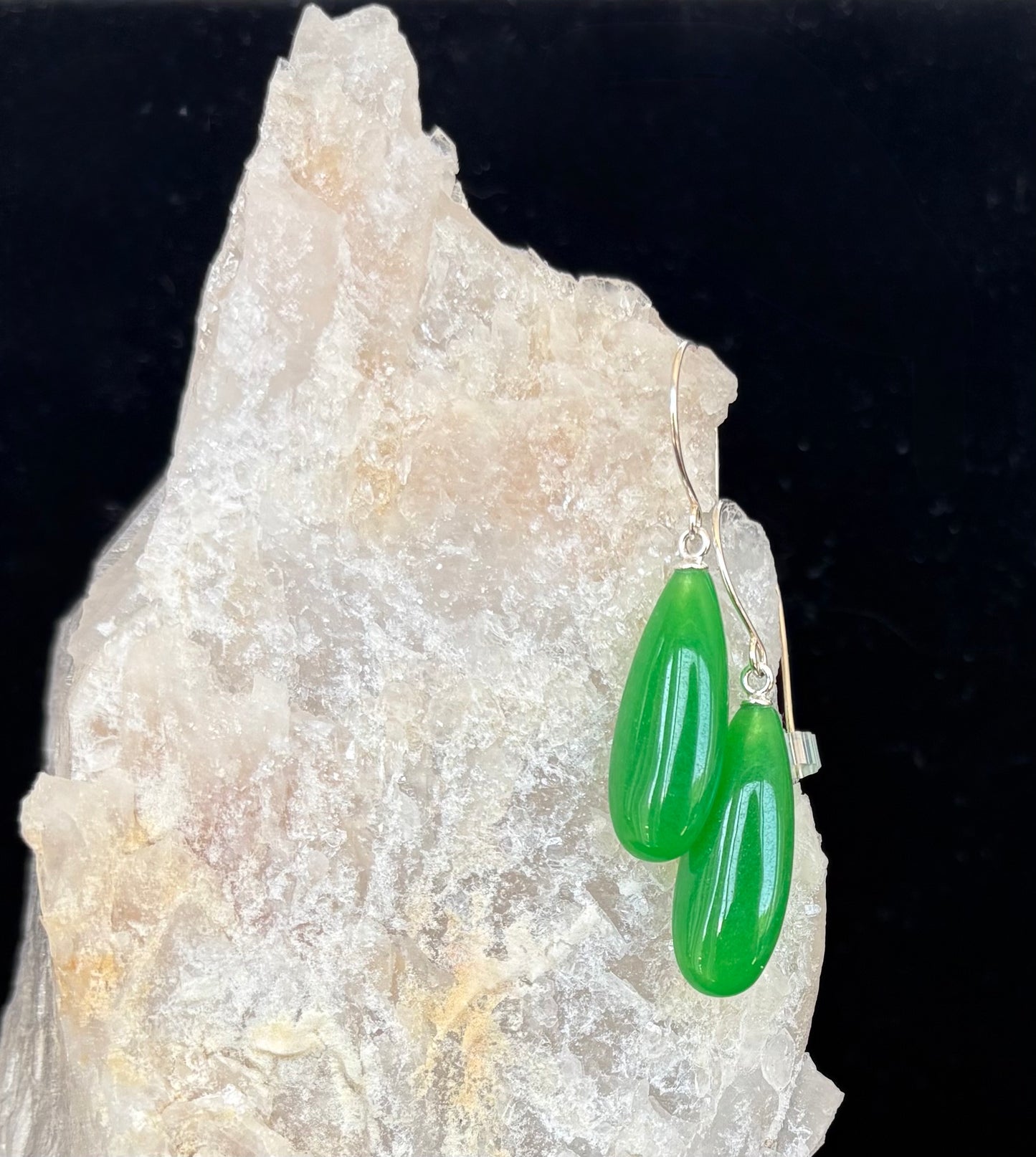 Green teardrop gemstone earrings on a rock with a dark background