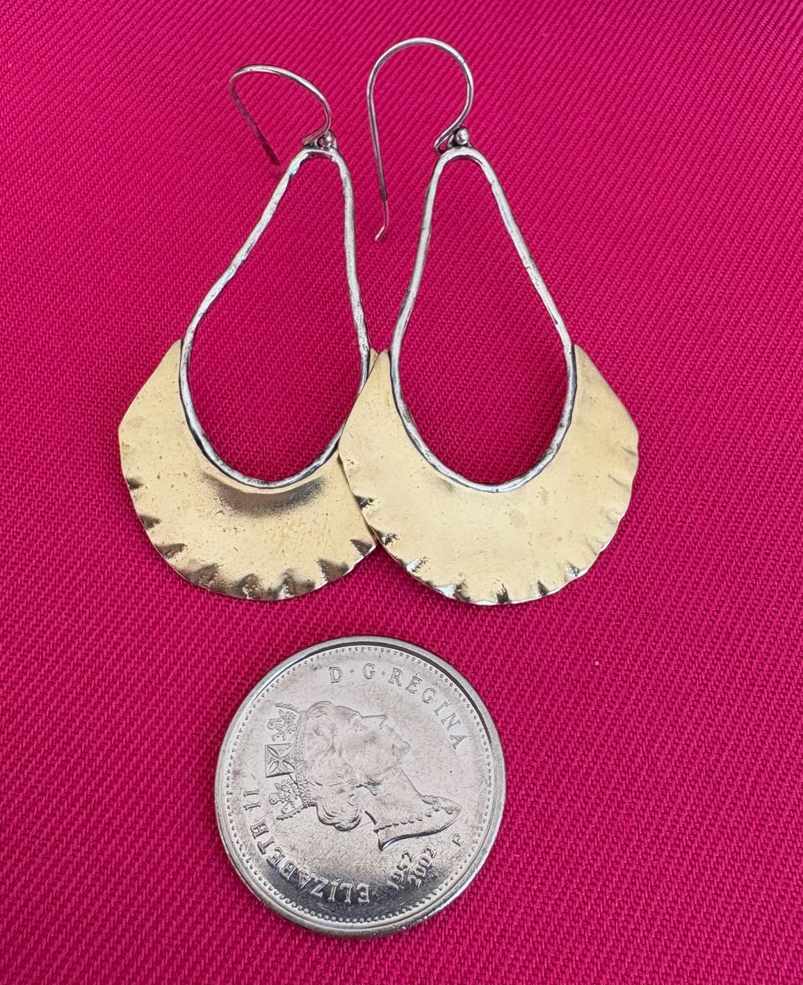 Gold and silver teardrop earrings on a pink background with a coin for scale.